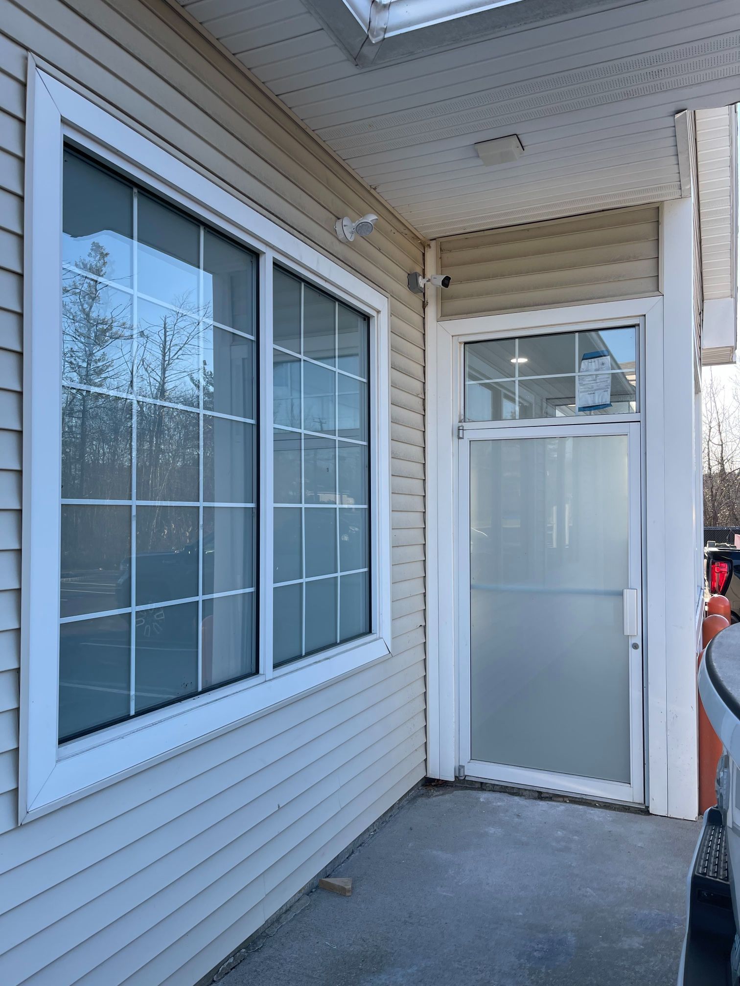 Exterior of a building with a large window and frosted glass door. Tan siding, white trim.