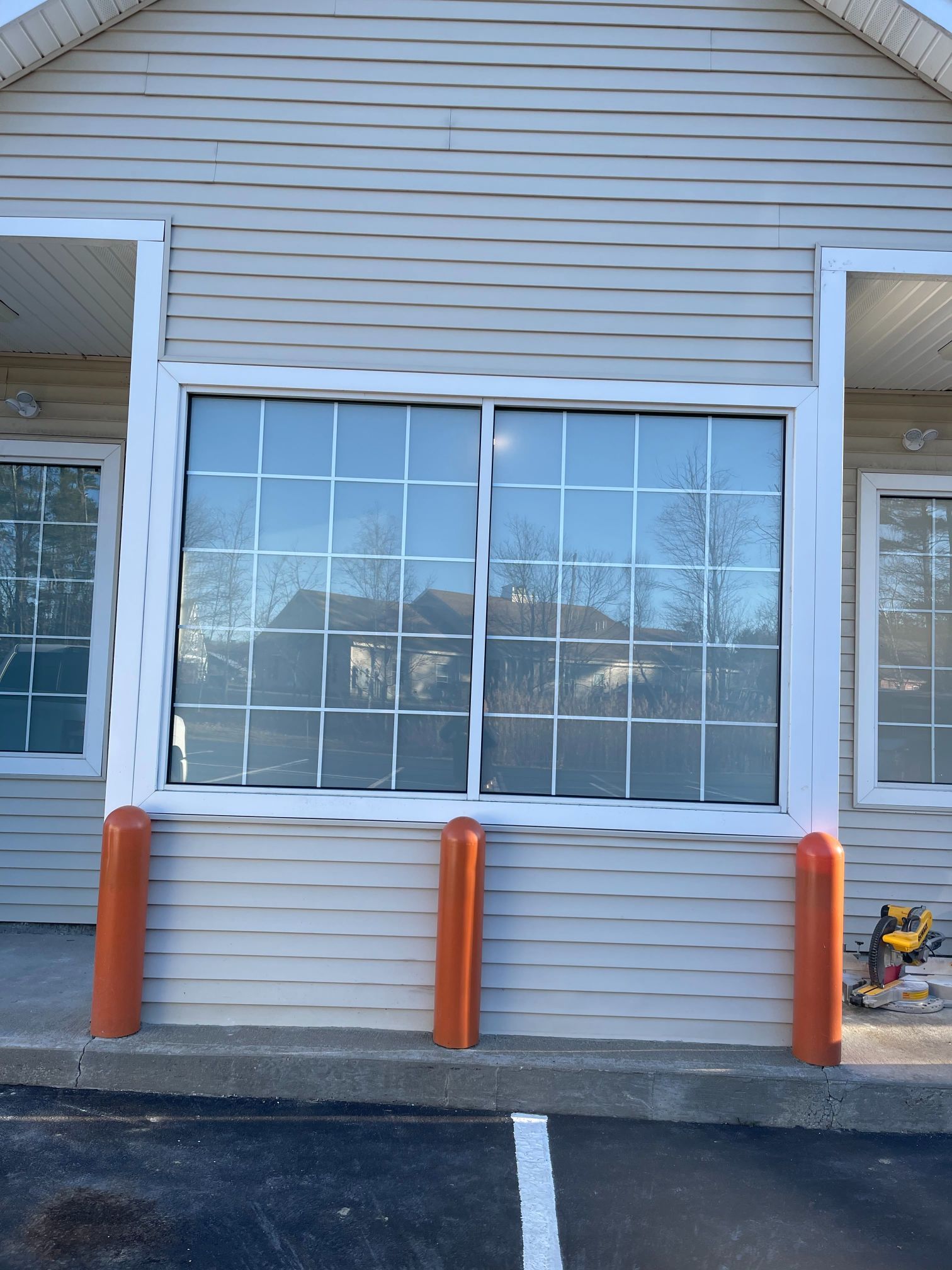 Building exterior with large sliding window, white trim, beige siding, and orange bollards.