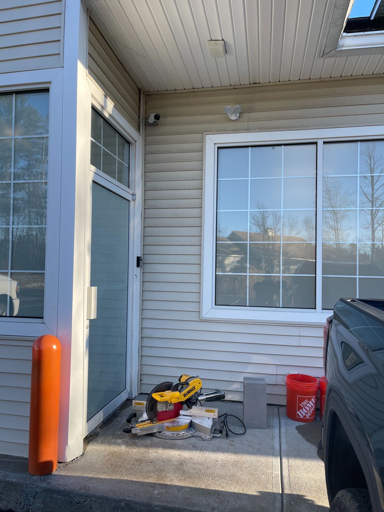 Exterior of a building with tools, door, and windows. Orange bollard, DeWalt tools, and a red bucket present.