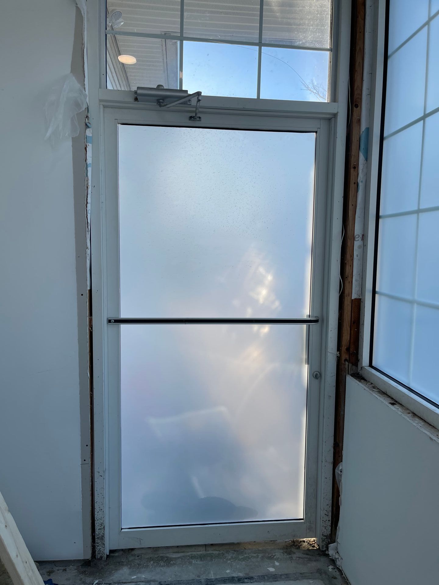 White door with frosted glass and a window above it, set between two walls.