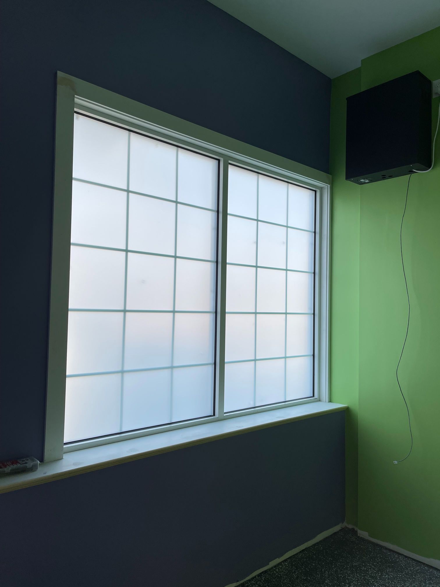 Window with frosted panes in a room with blue and green walls. A black box is mounted on the wall.