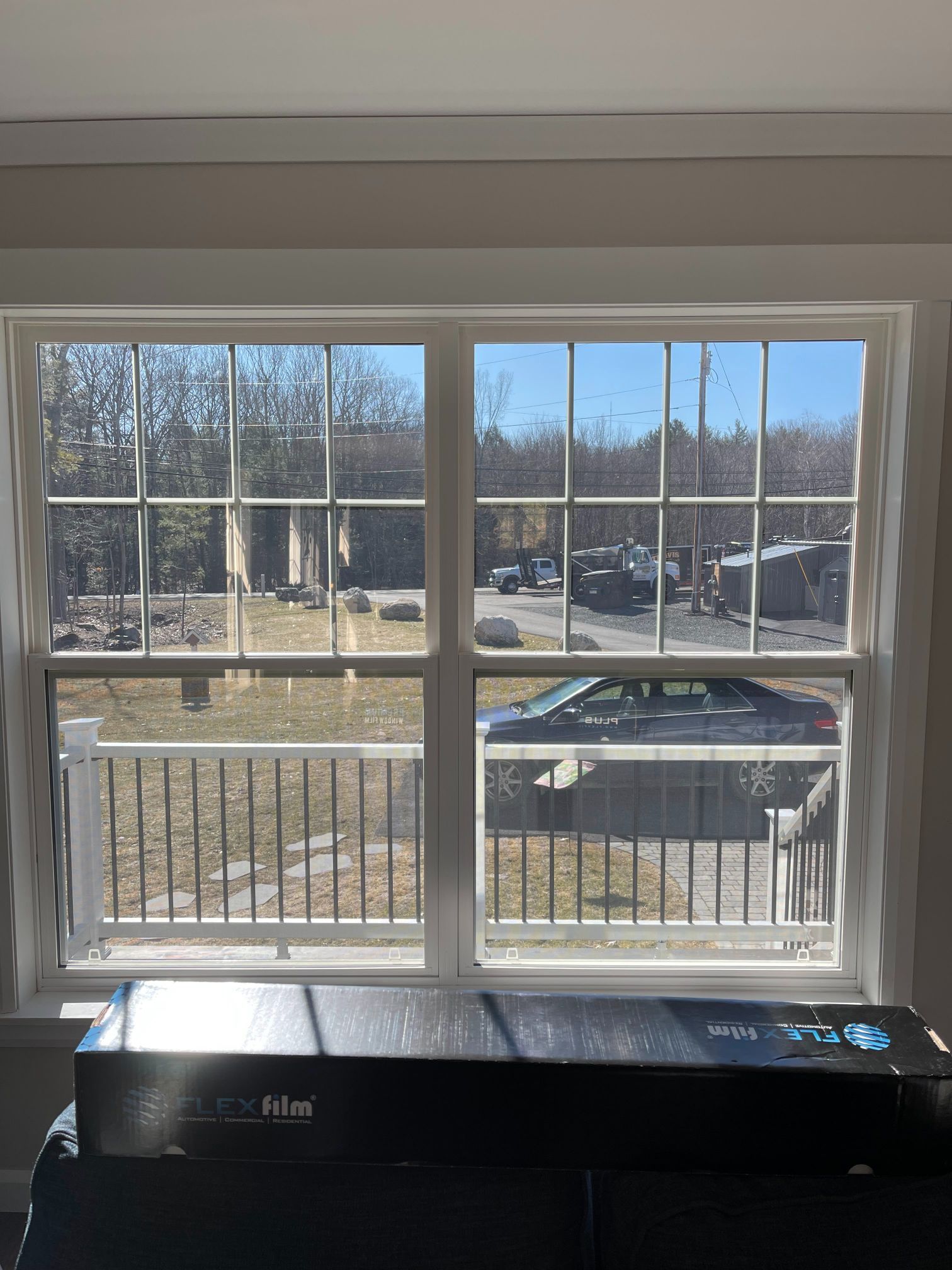 Window with multi-pane design, overlooking a yard with cars, trees, and a white fence. Window film box sits below.