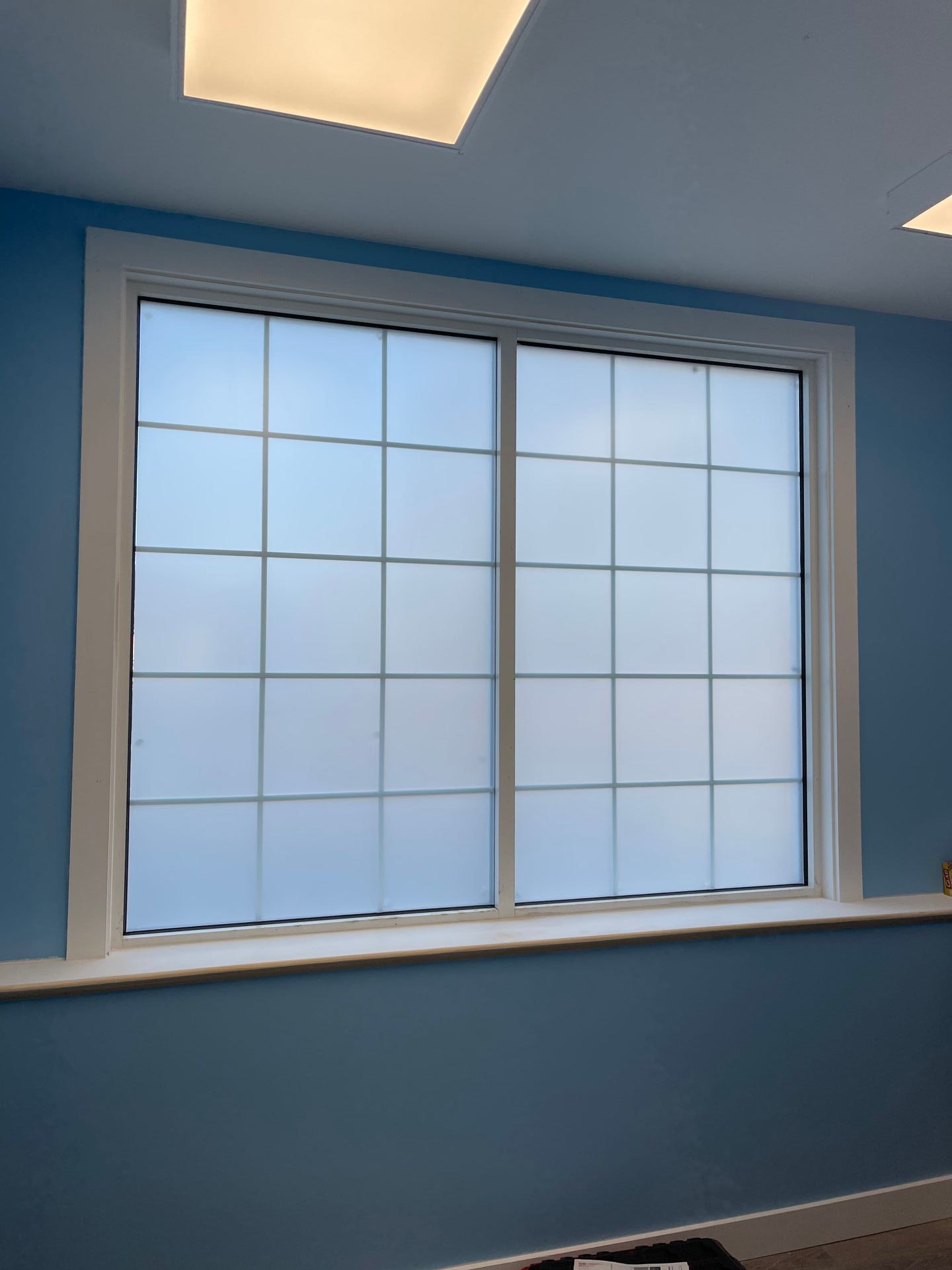 Large window with white grid pattern against frosted glass, set in a blue room with white trim and a windowsill.