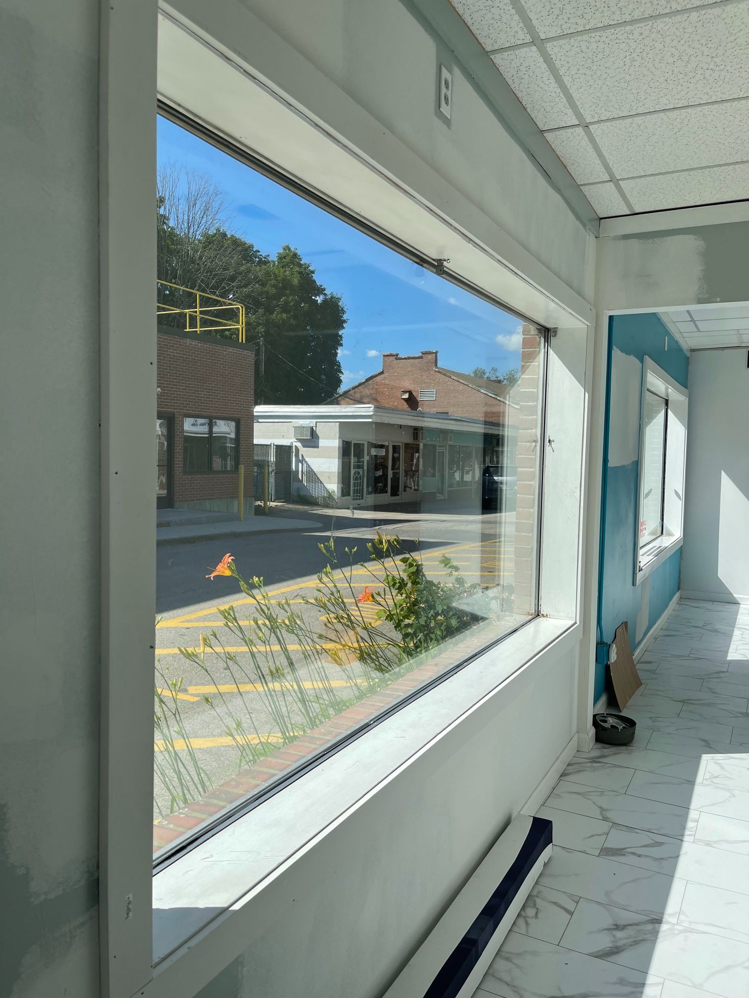 Interior view through a large window. A street scene is visible; a building and sky reflected in the glass.