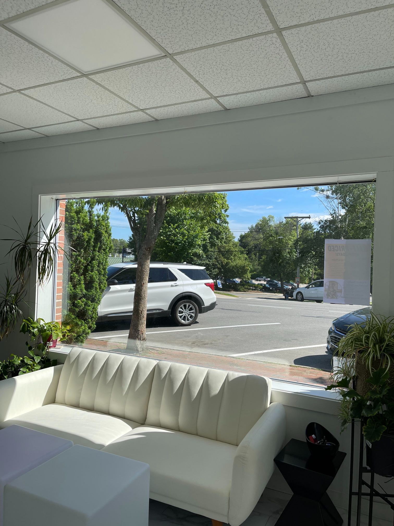 Interior view through a large window overlooking a parking lot with cars. A white sofa sits inside.