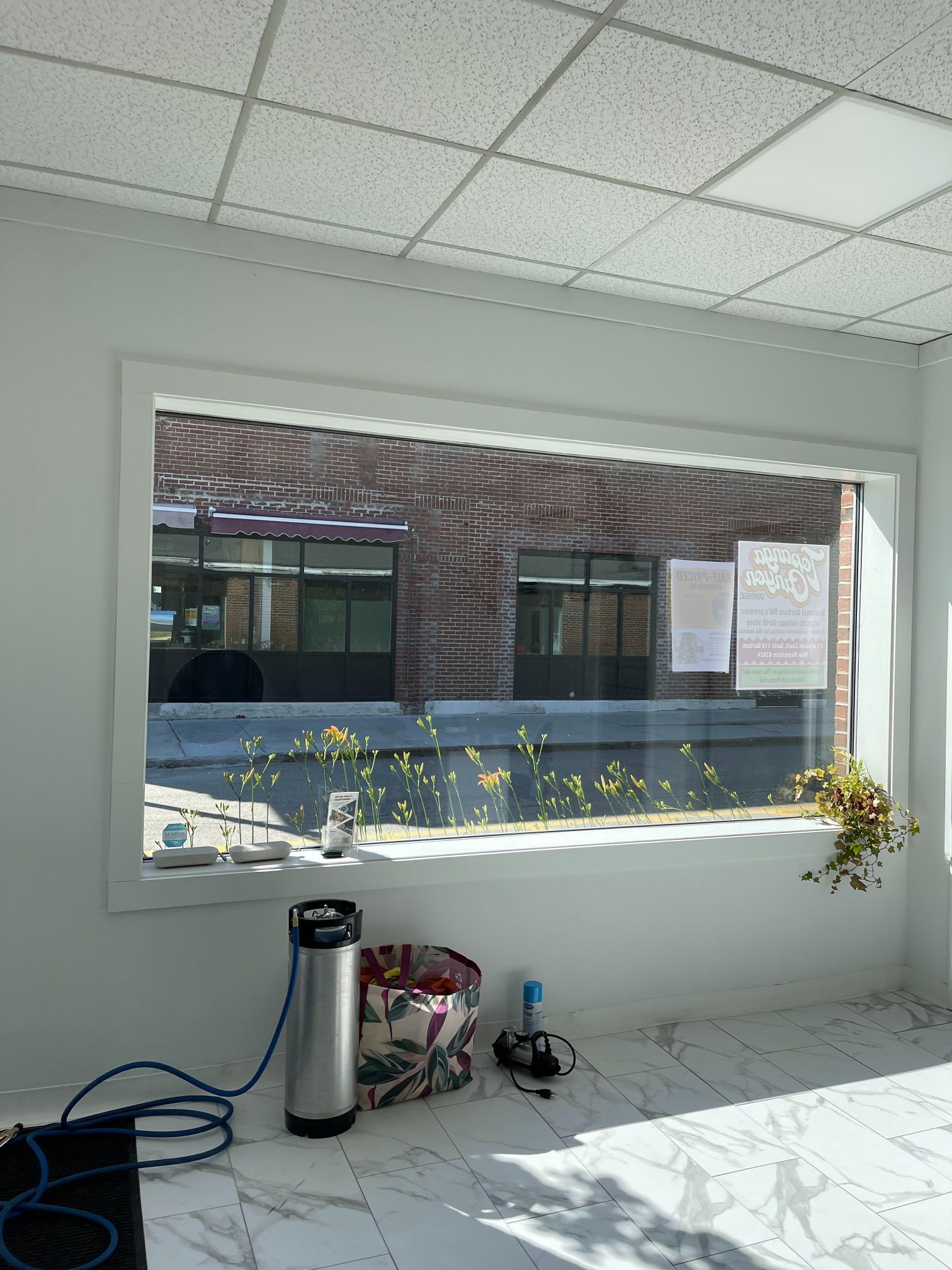 A rectangular window with a brick building visible outside. Inside: a keg, trash, and tiled floor.