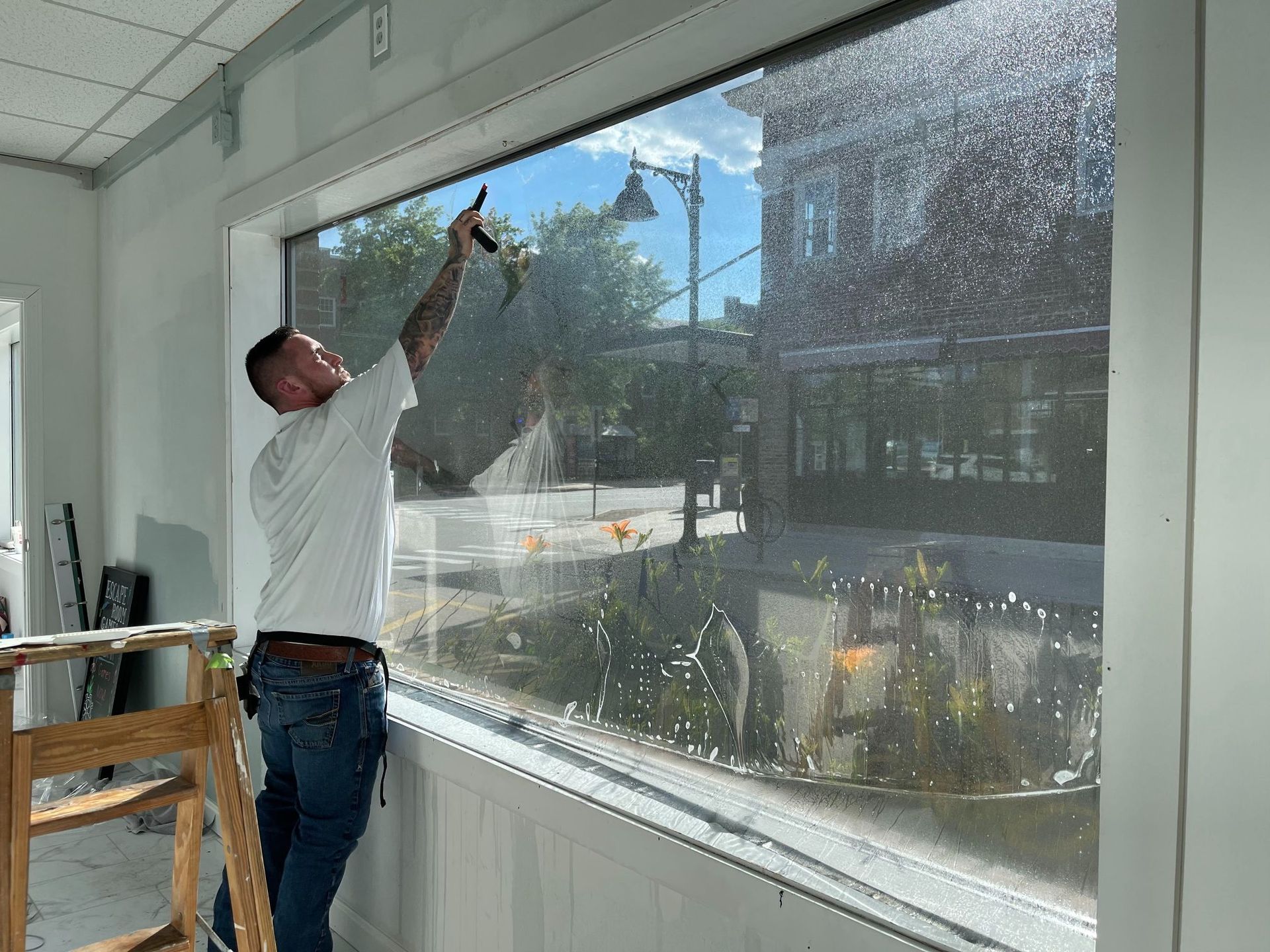 Person squeegeeing a large, wet window; a street scene is visible through it.