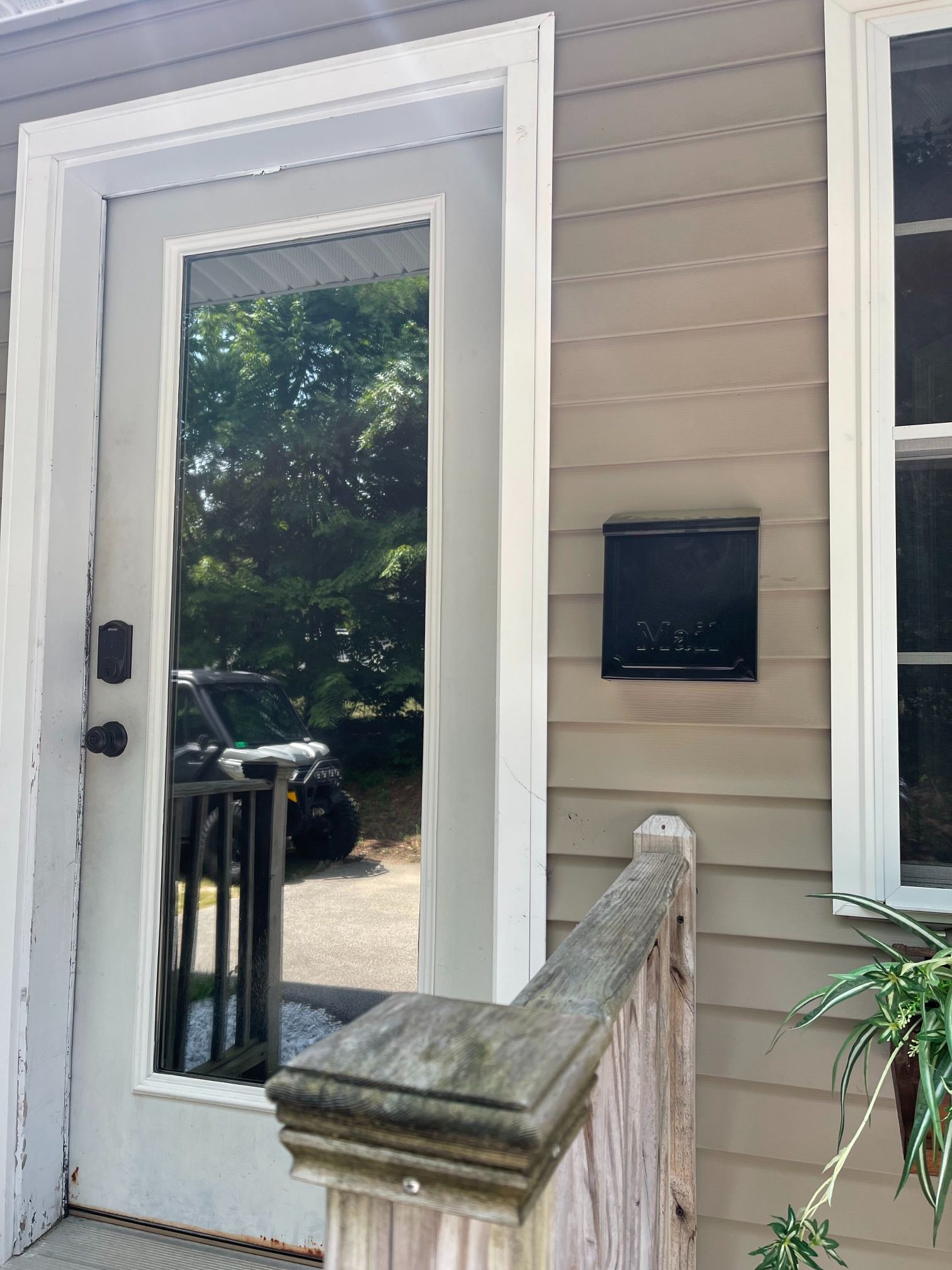 A black mailbox on a light brown house exterior next to a white door with a reflective window.