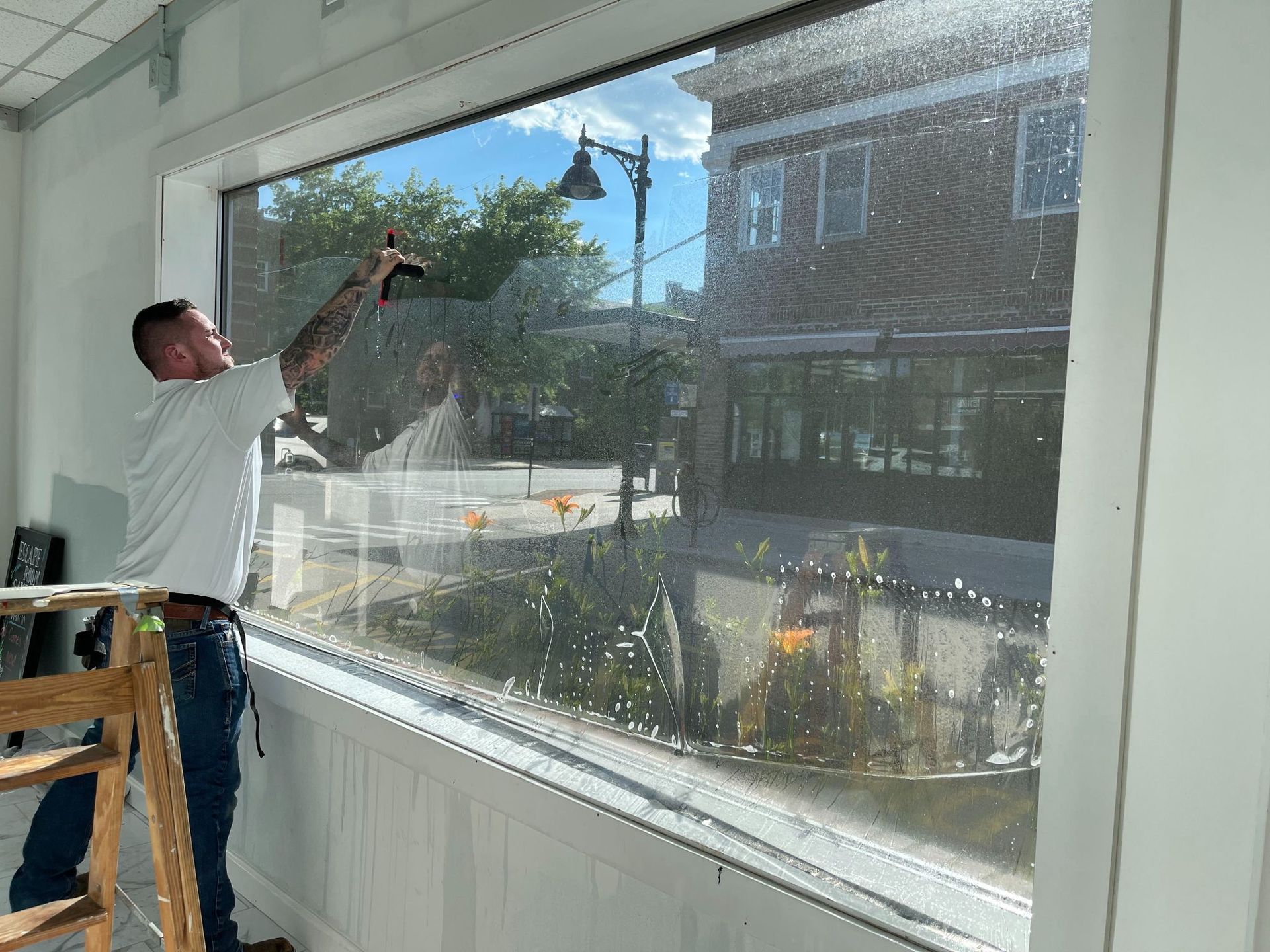 Man applying window film inside a building with a street view. He is using a squeegee.