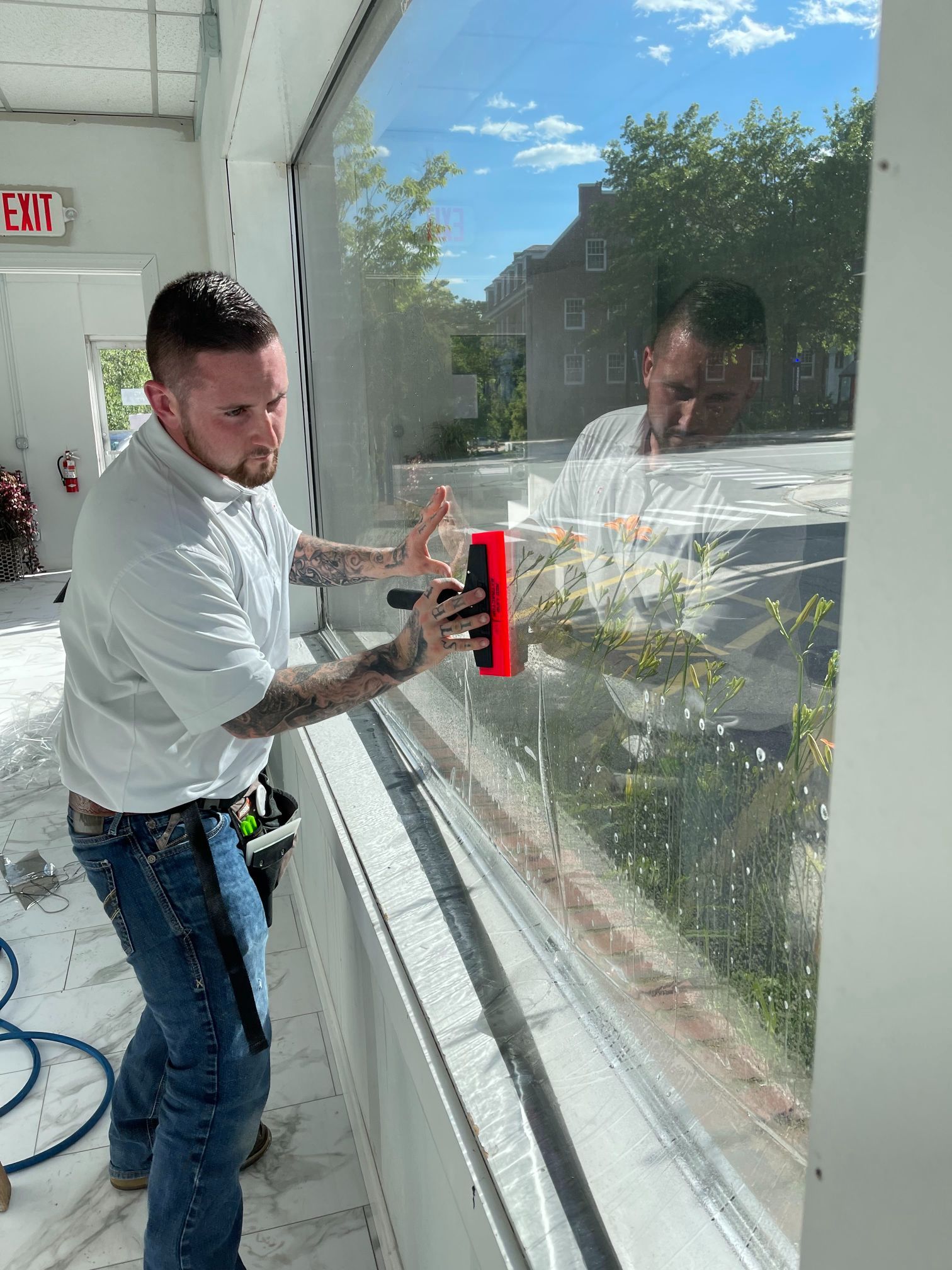 Man installing window film on a storefront window, using a red squeegee.