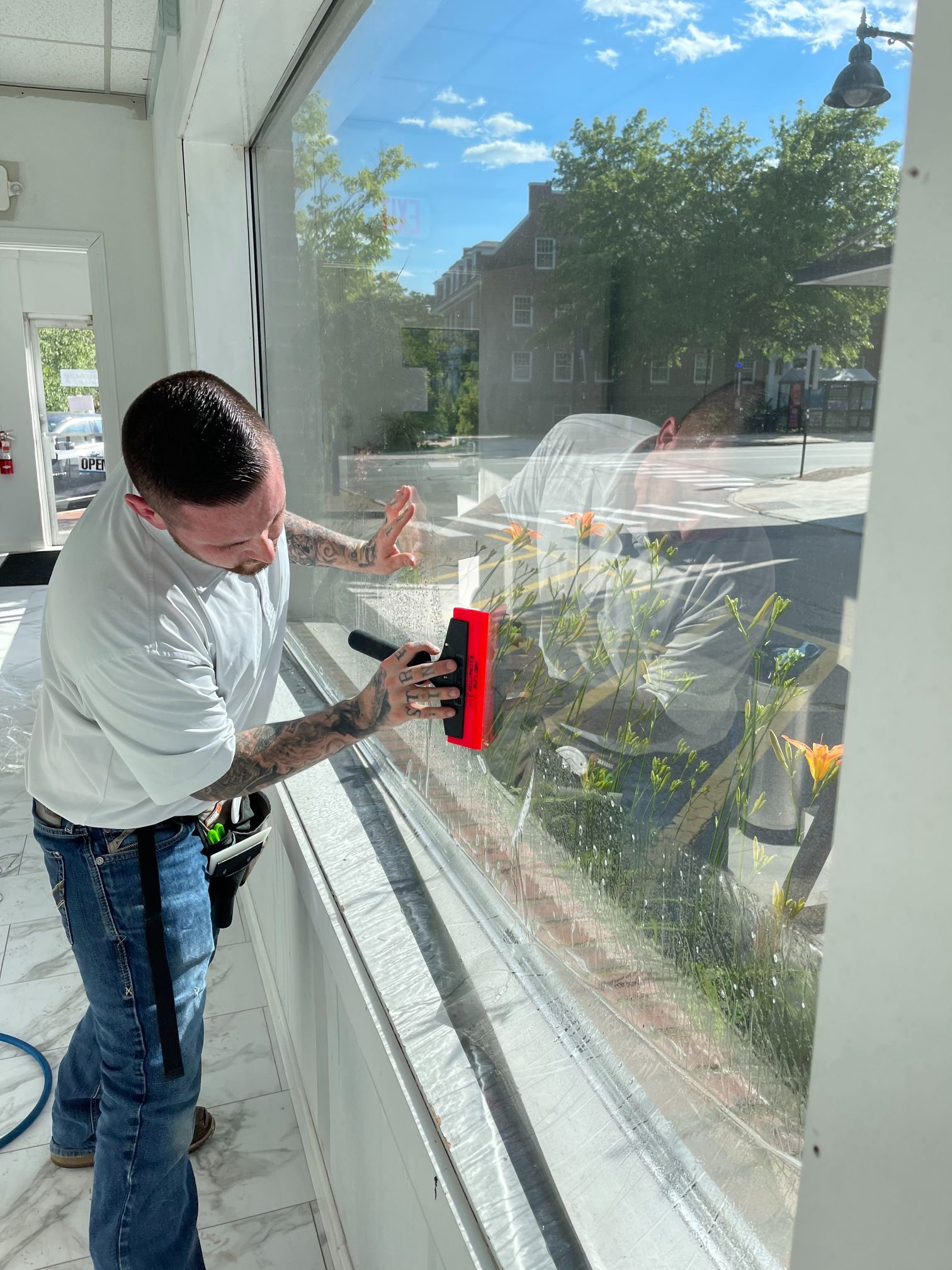 Man applying film to a window with a squeegee. Outdoors on a sunny day.