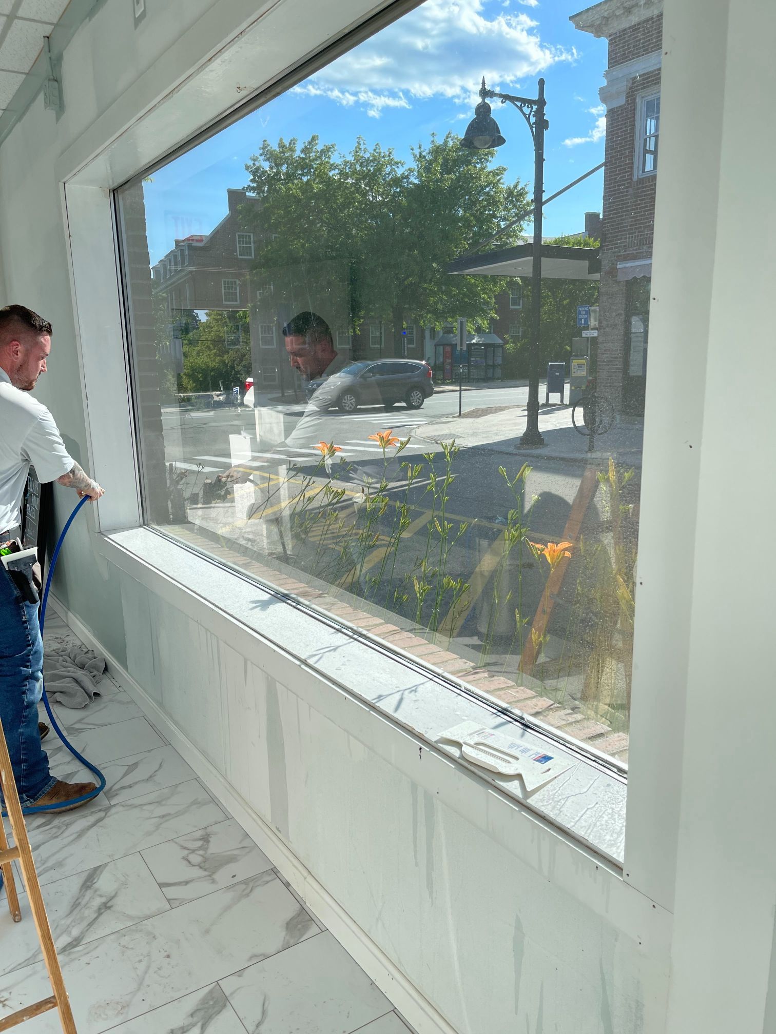 Man cleaning a large window with a spray bottle, reflecting street scene.