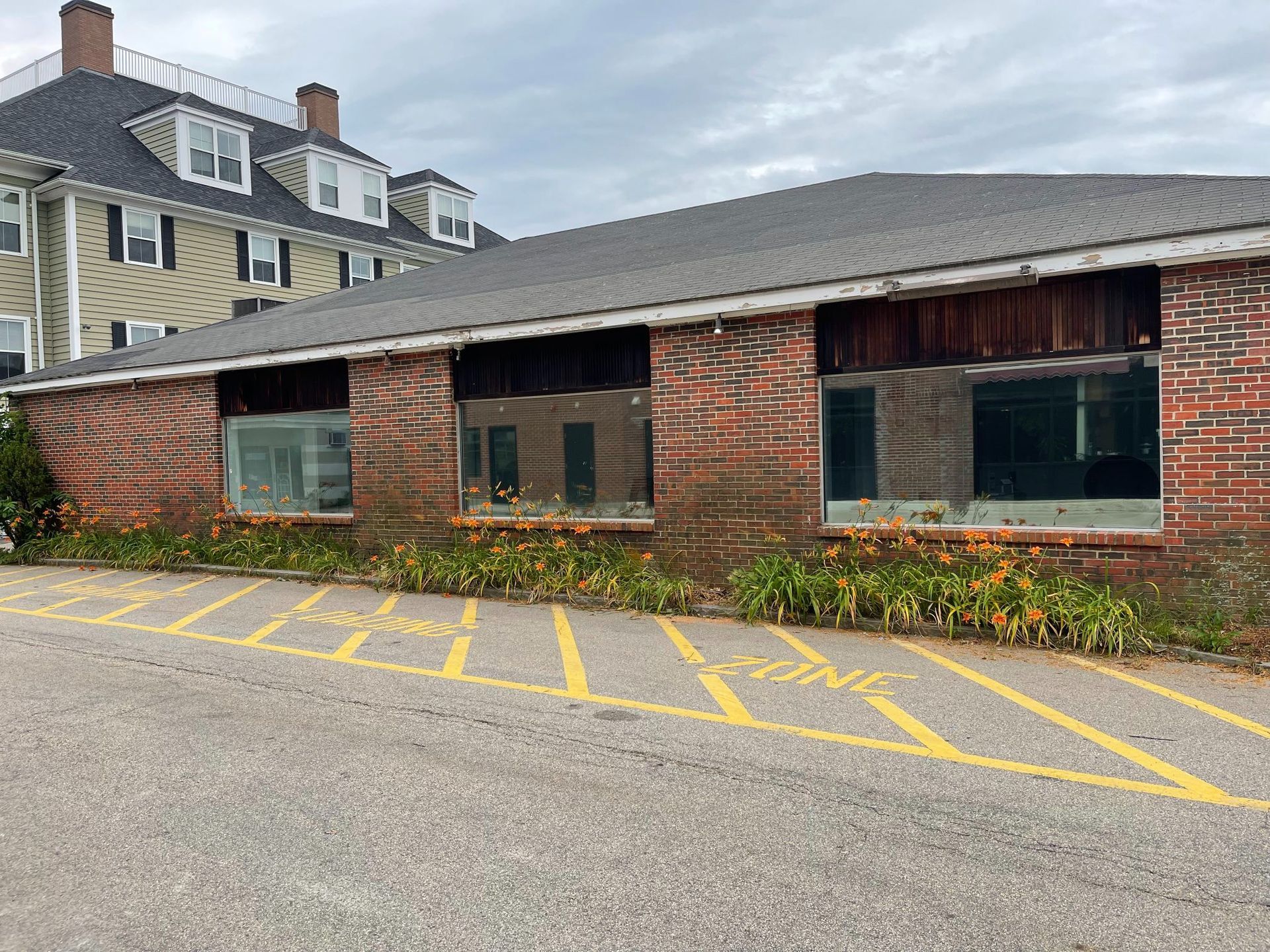 Brick building with empty window frames and a parking zone in front.