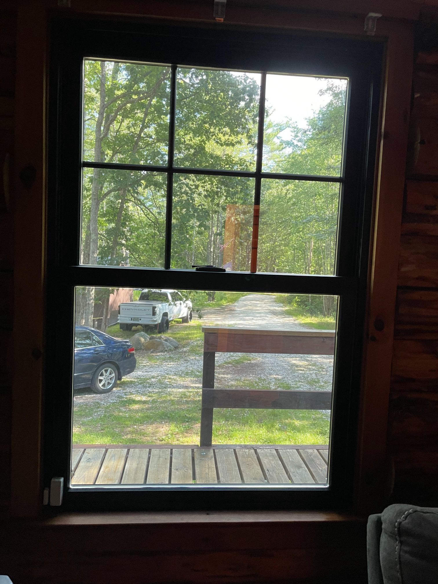 Window view of a gravel driveway, trees, and parked cars; inside a cabin with wood walls.