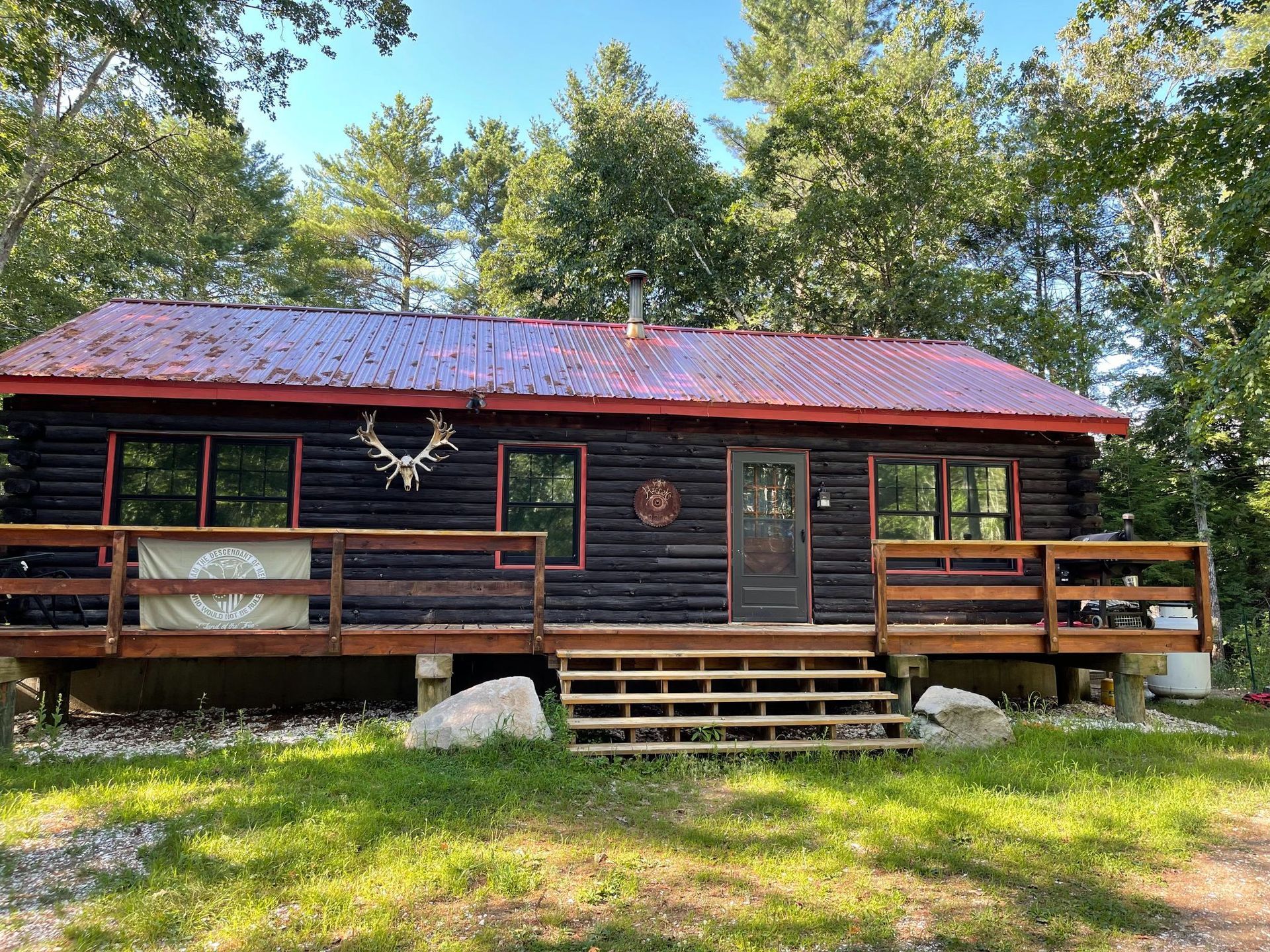 Log cabin with a red roof and wooden deck surrounded by trees.