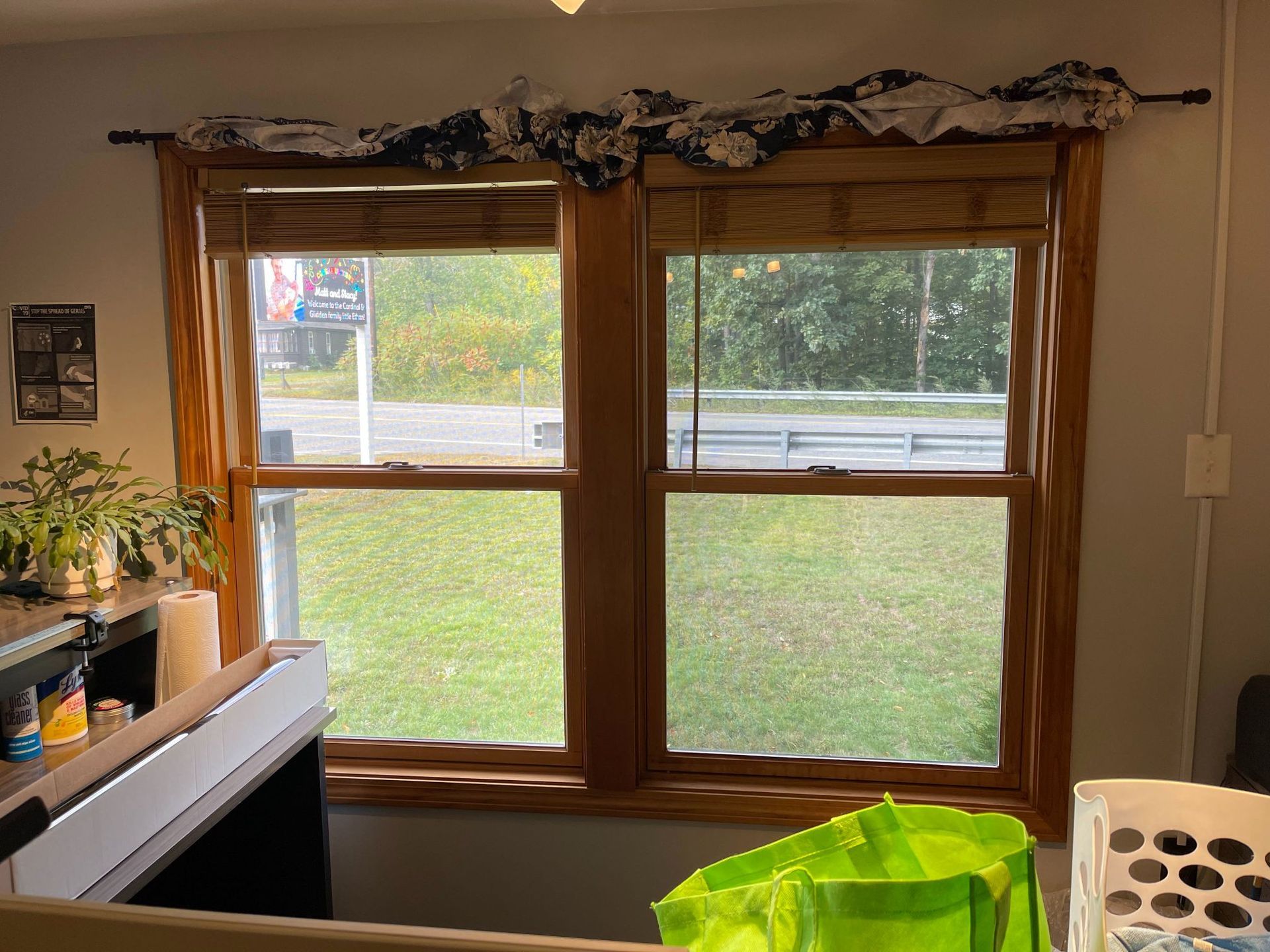 Two wooden framed windows with green yard view, bamboo shades, and decorative fabric valance.