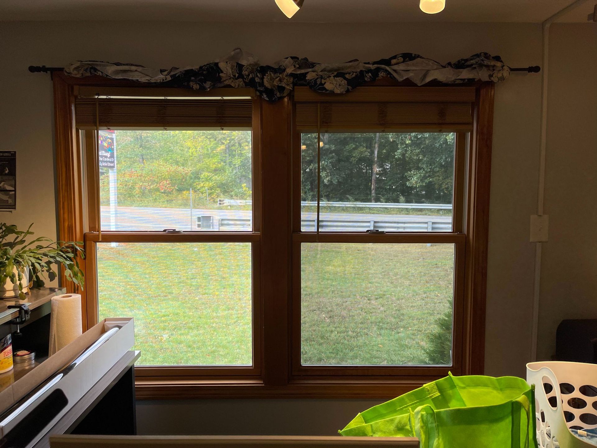 Two pane window with wooden trim, looking out onto green grass and a road, decorated with bamboo blinds and a 