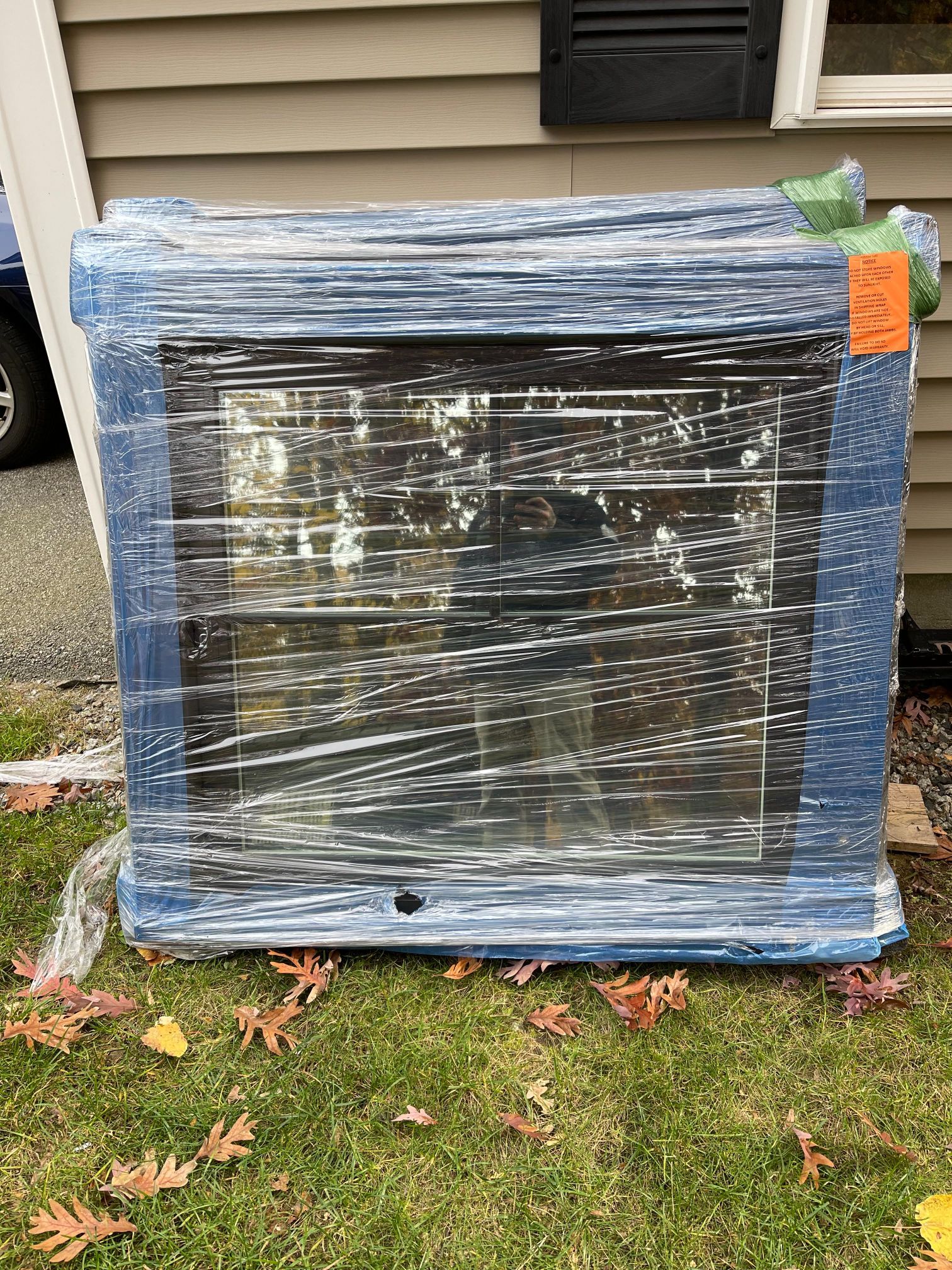 Wrapped oven leaning against a beige house on green grass with fall leaves.