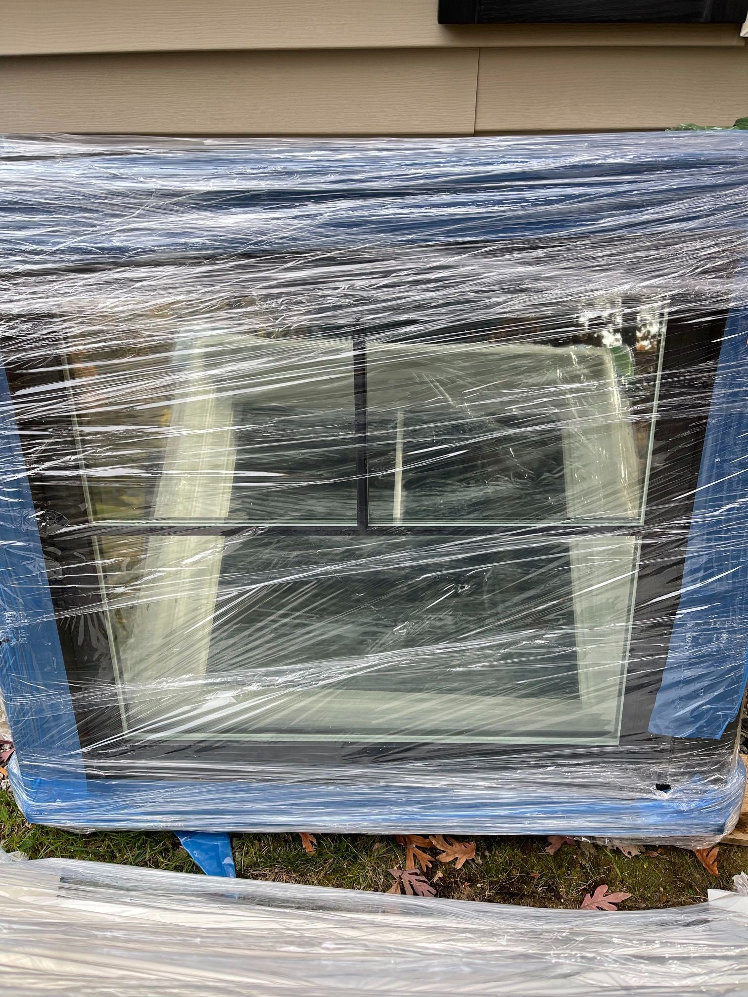 Window wrapped in blue tape and plastic. Black grid design across the glass.