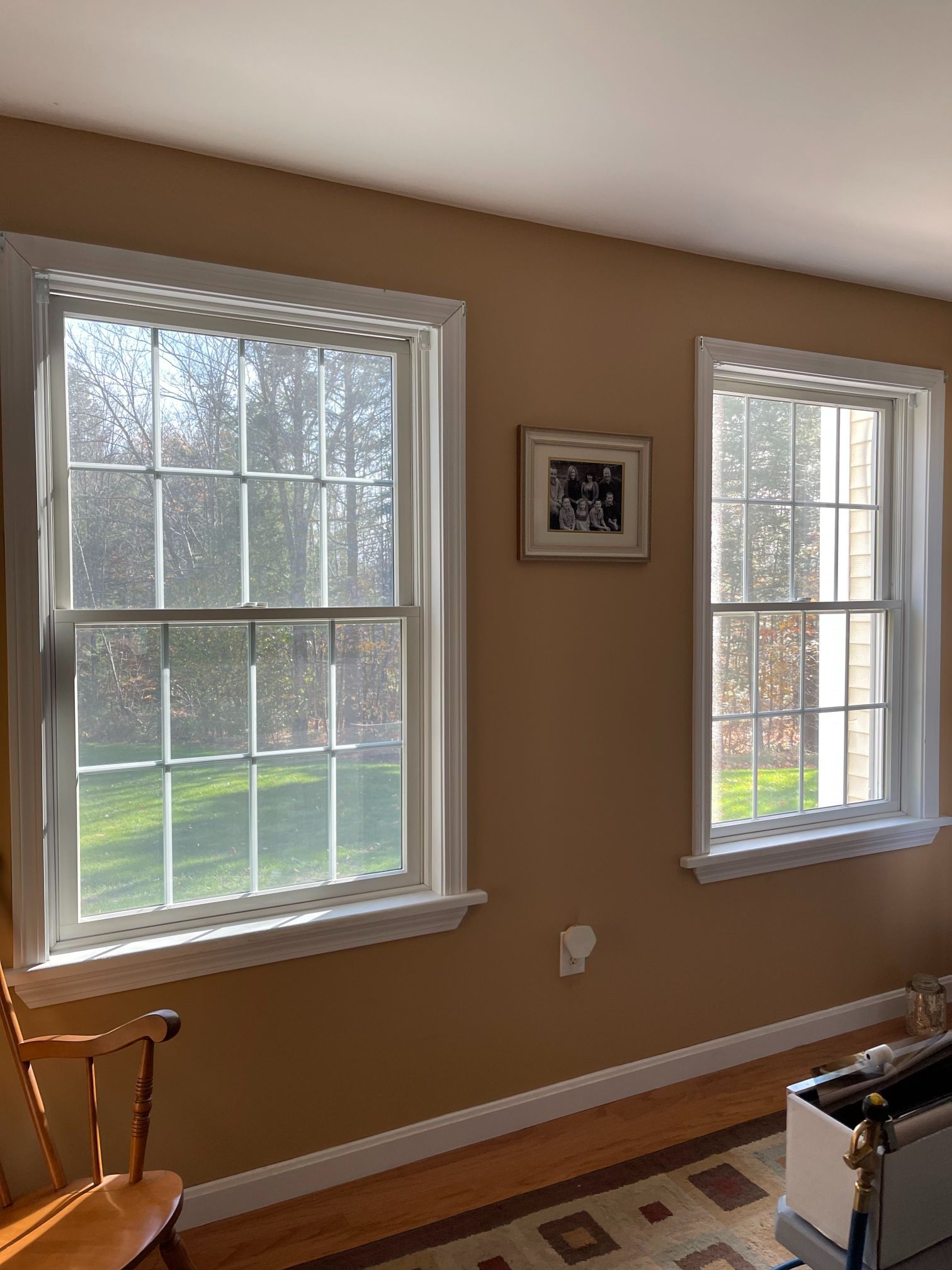 Two white-framed windows on a tan wall. A photo hangs between them. Sunlight streams in.