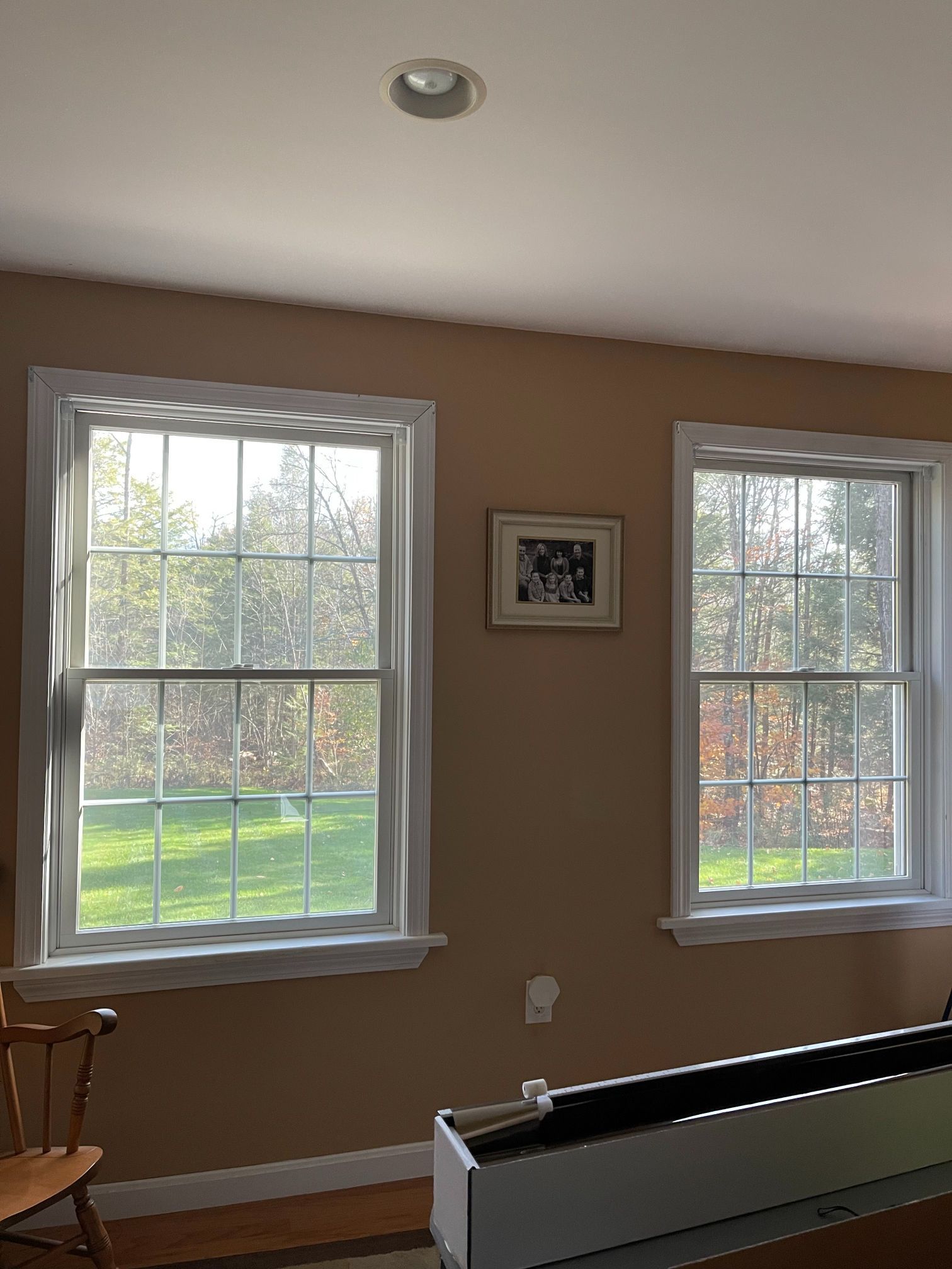 Two white-framed windows on tan wall, small photo, white radiator, chair visible. Sunlight, outdoors.