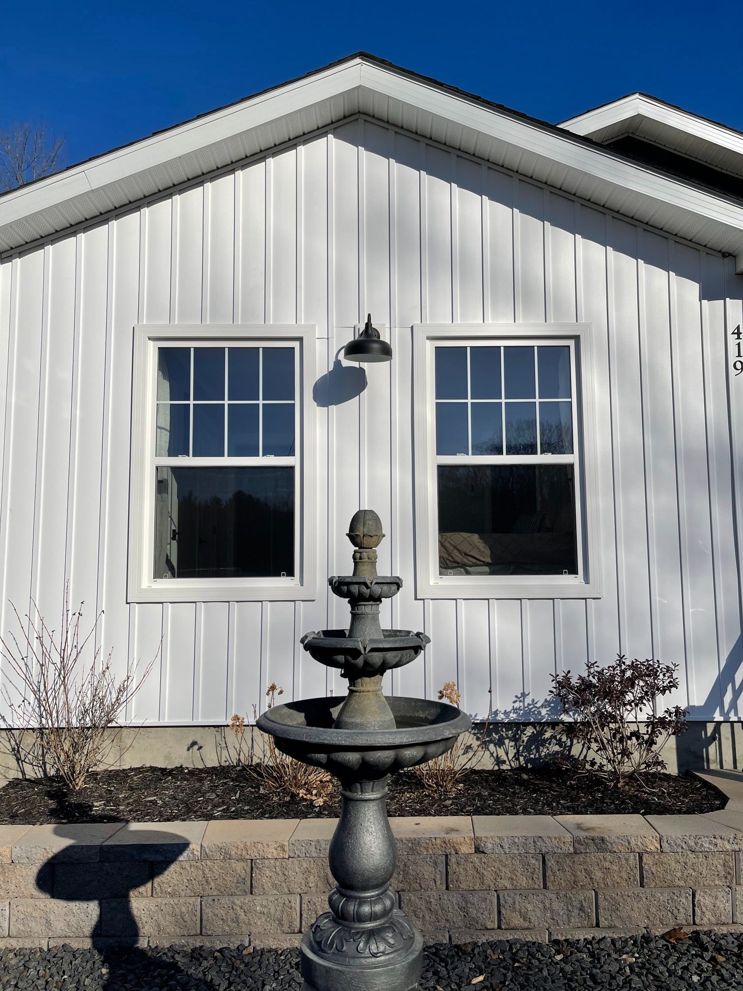 White farmhouse with two windows and a fountain in front.