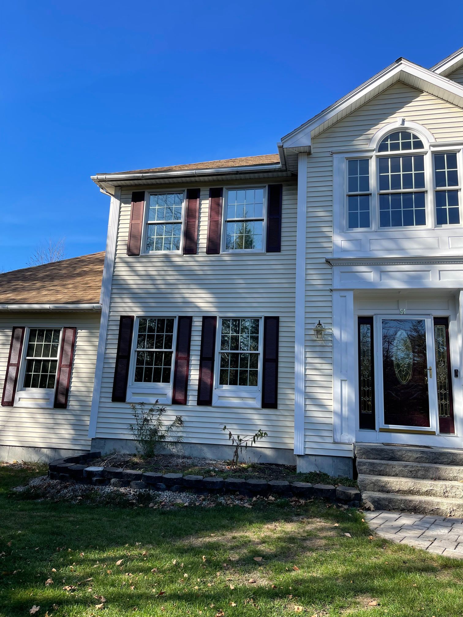 Two-story house with tan siding, burgundy shutters, and a clear blue sky.