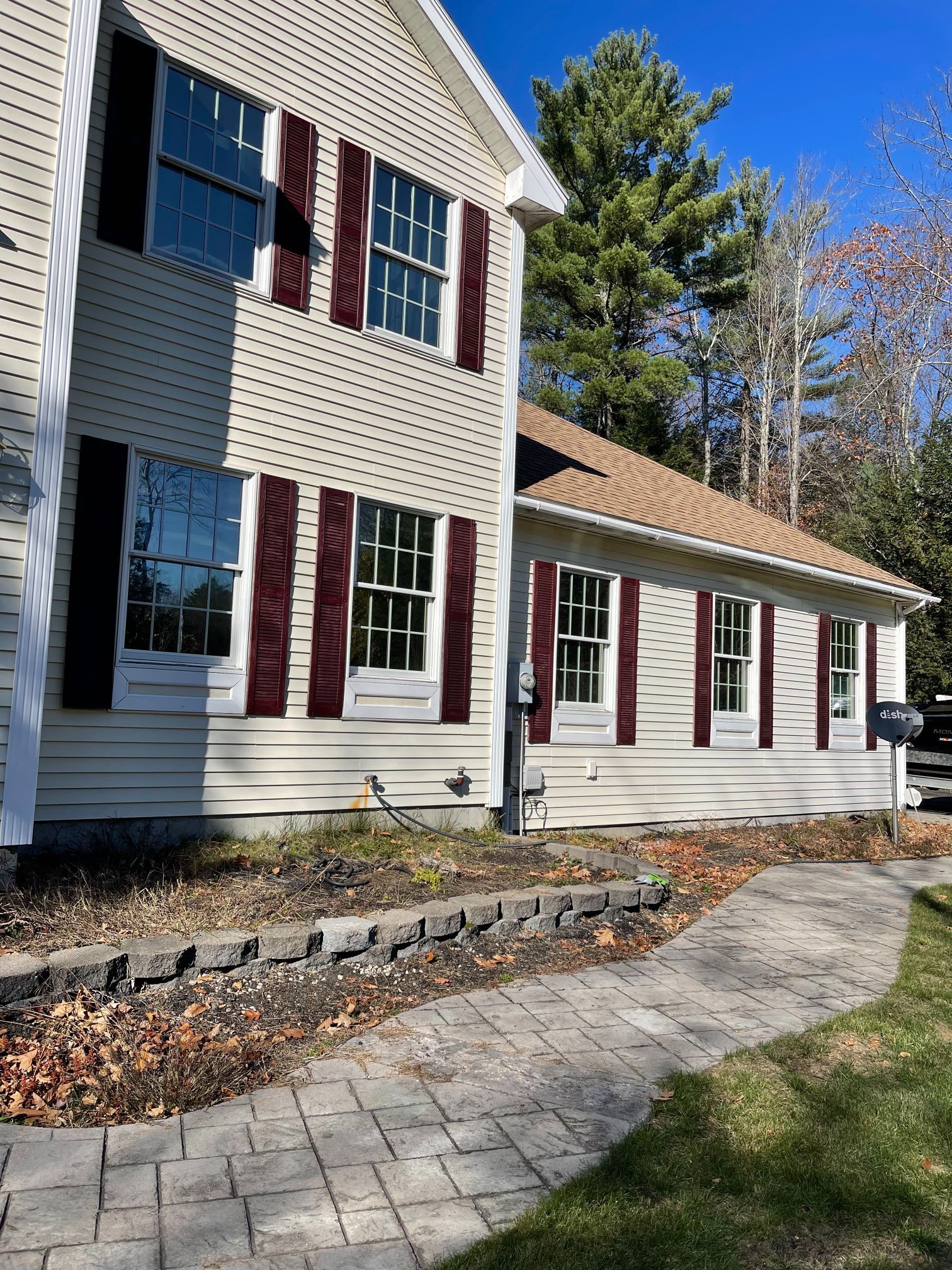Beige house with burgundy shutters, a brick walkway, and a landscaped border.