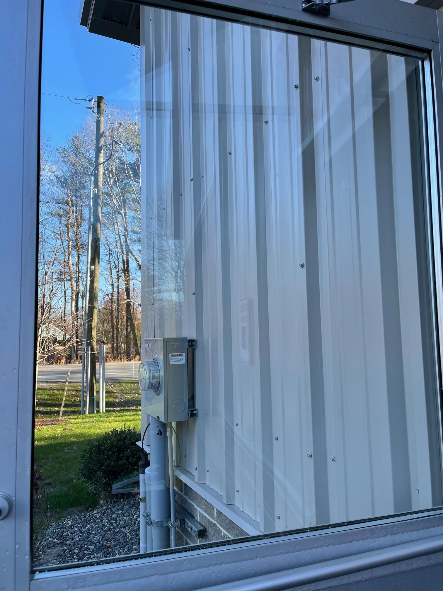 Window view of a metal building, utility box, trees, and sky.