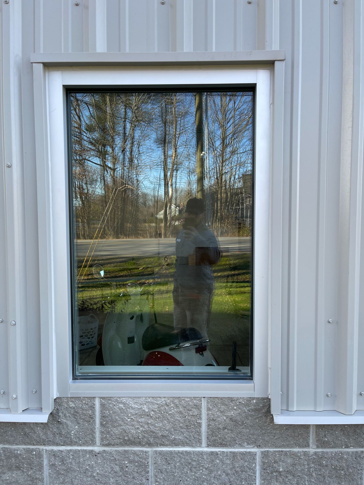 Window in a gray building reflects a person, trees, and a green lawn.