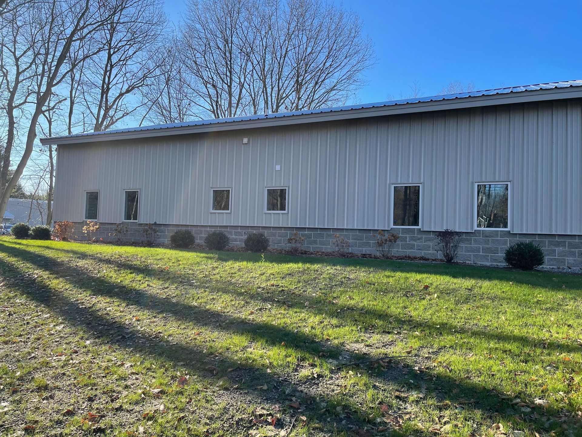Gray metal-sided building with several windows, stone foundation, and a grassy lawn.