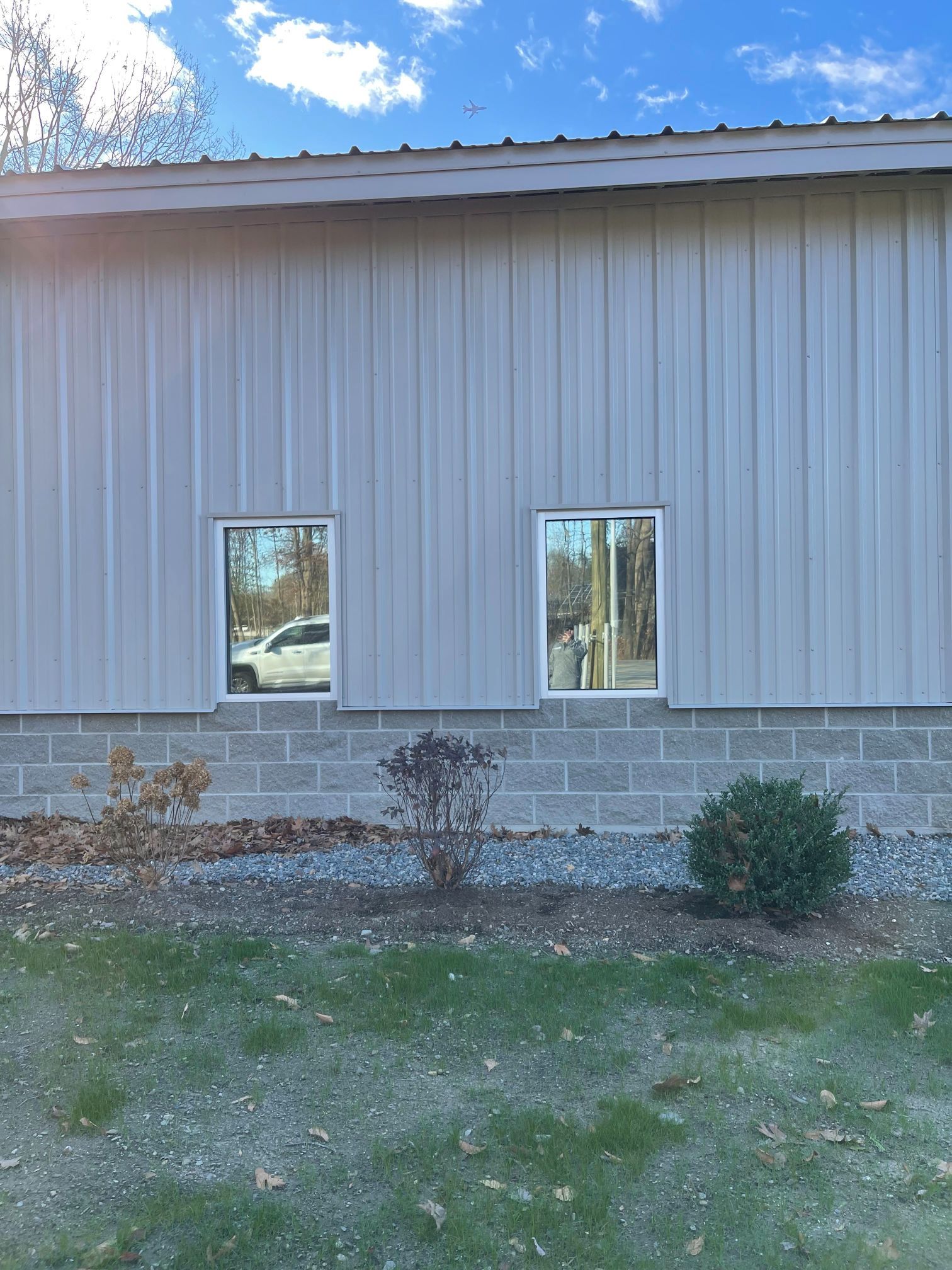 Exterior of a gray metal-sided building with two windows above a concrete block foundation and landscaping.