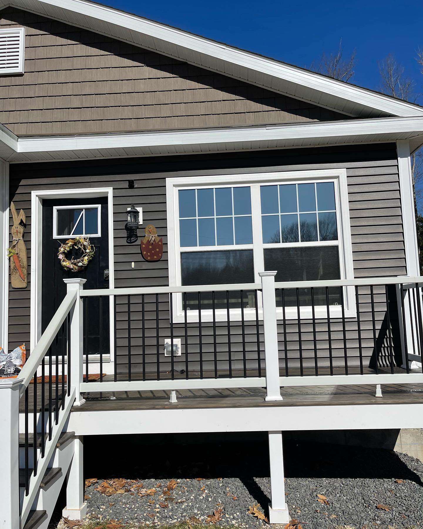 Gray house with white trim, black door with wreath, large window, and small porch.
