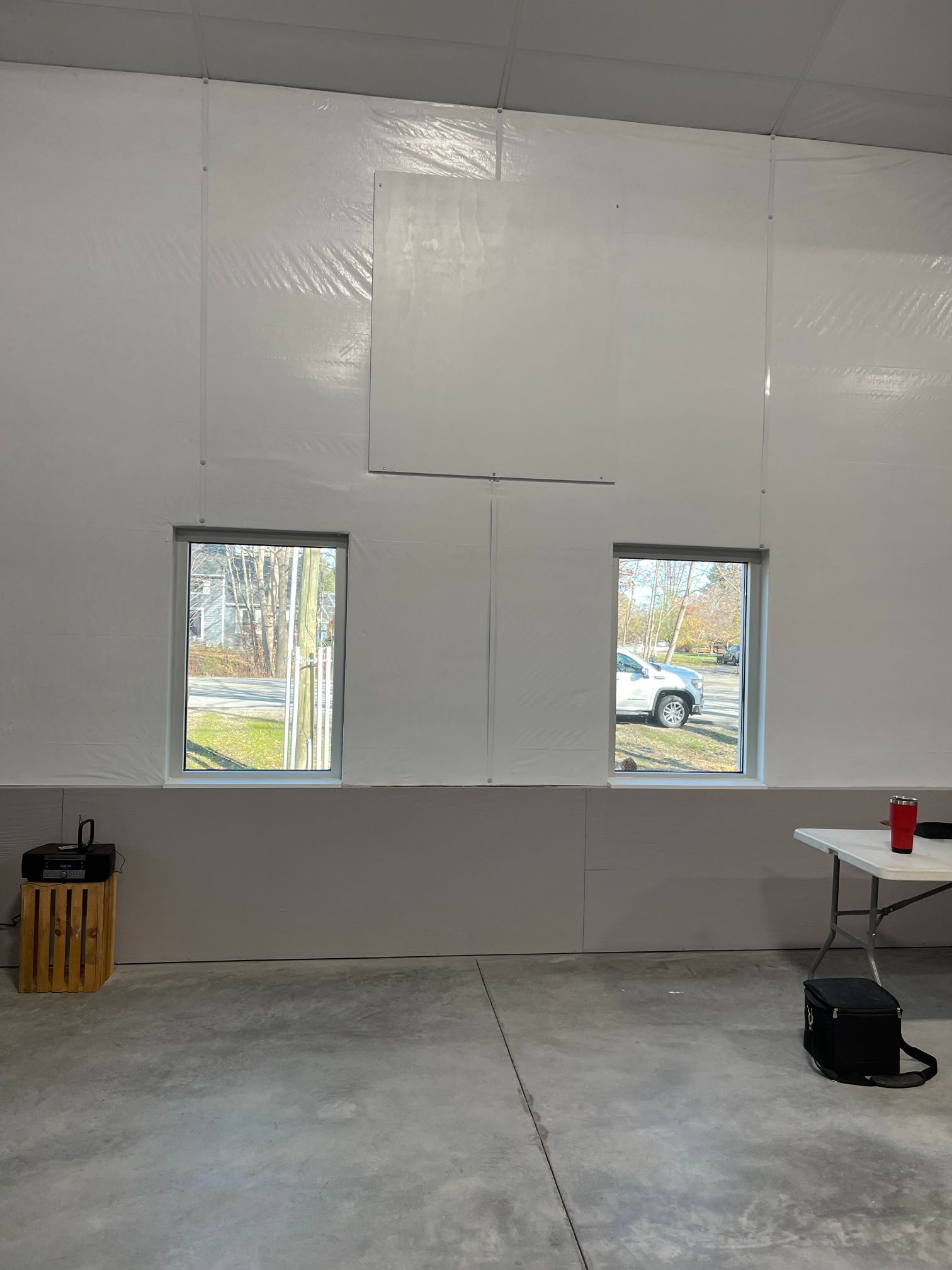 Interior of a white-walled building with two windows. A concrete floor and a wooden box are visible.