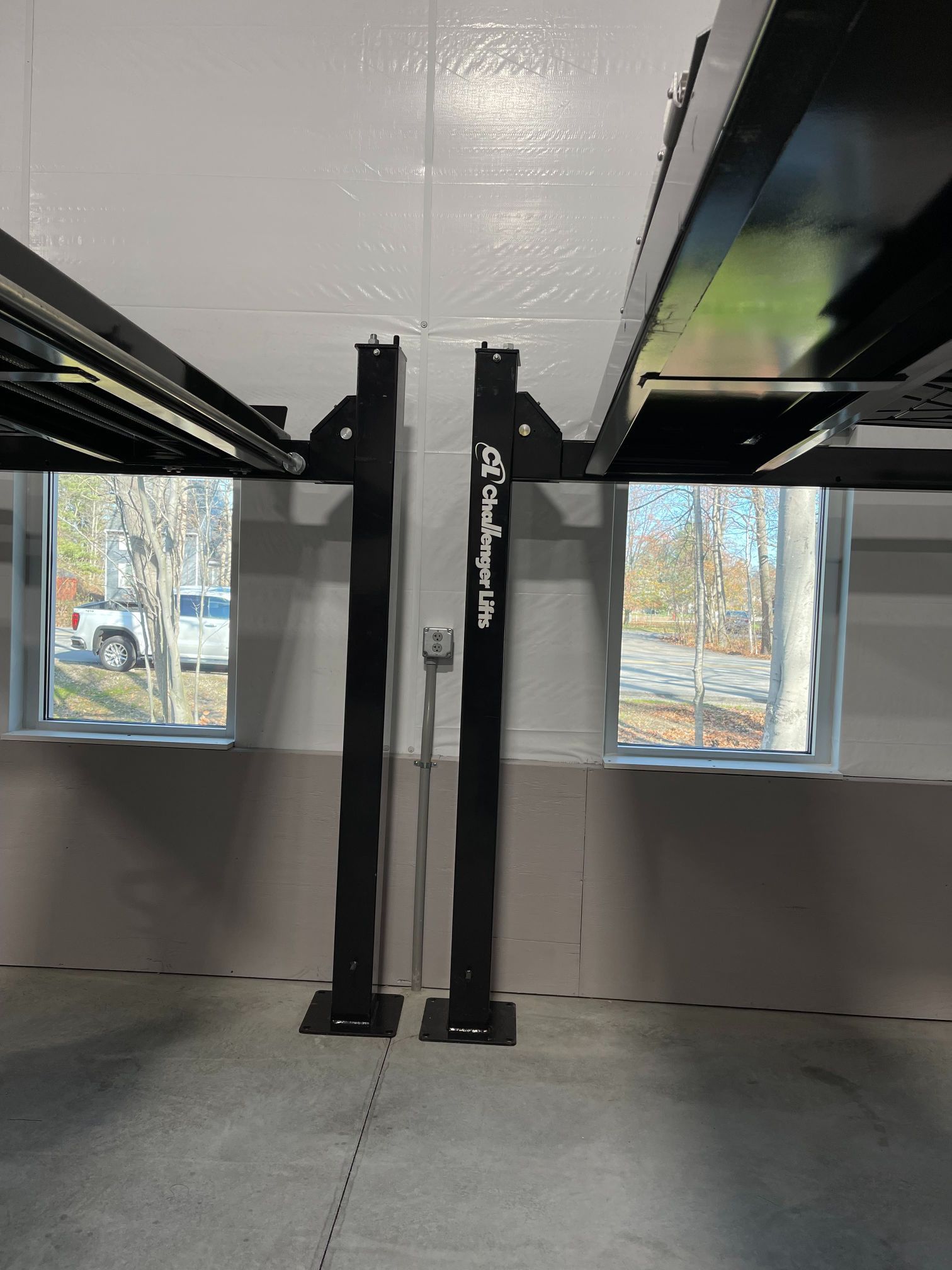 Garage four-post car lift installed in a room with two windows. Lift is black; walls are white and gray.