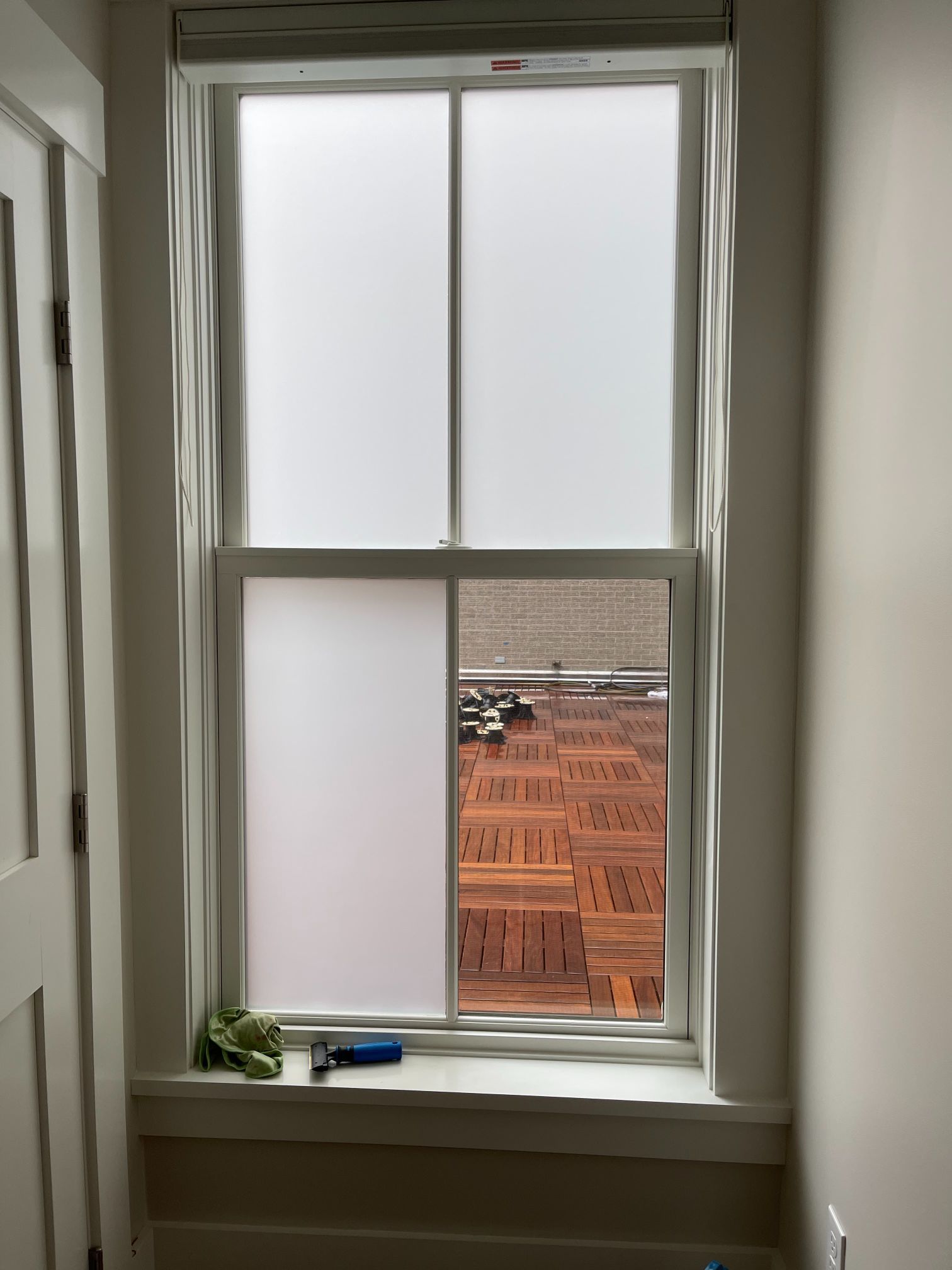 Window with frosted film partially covering glass, revealing exterior construction.