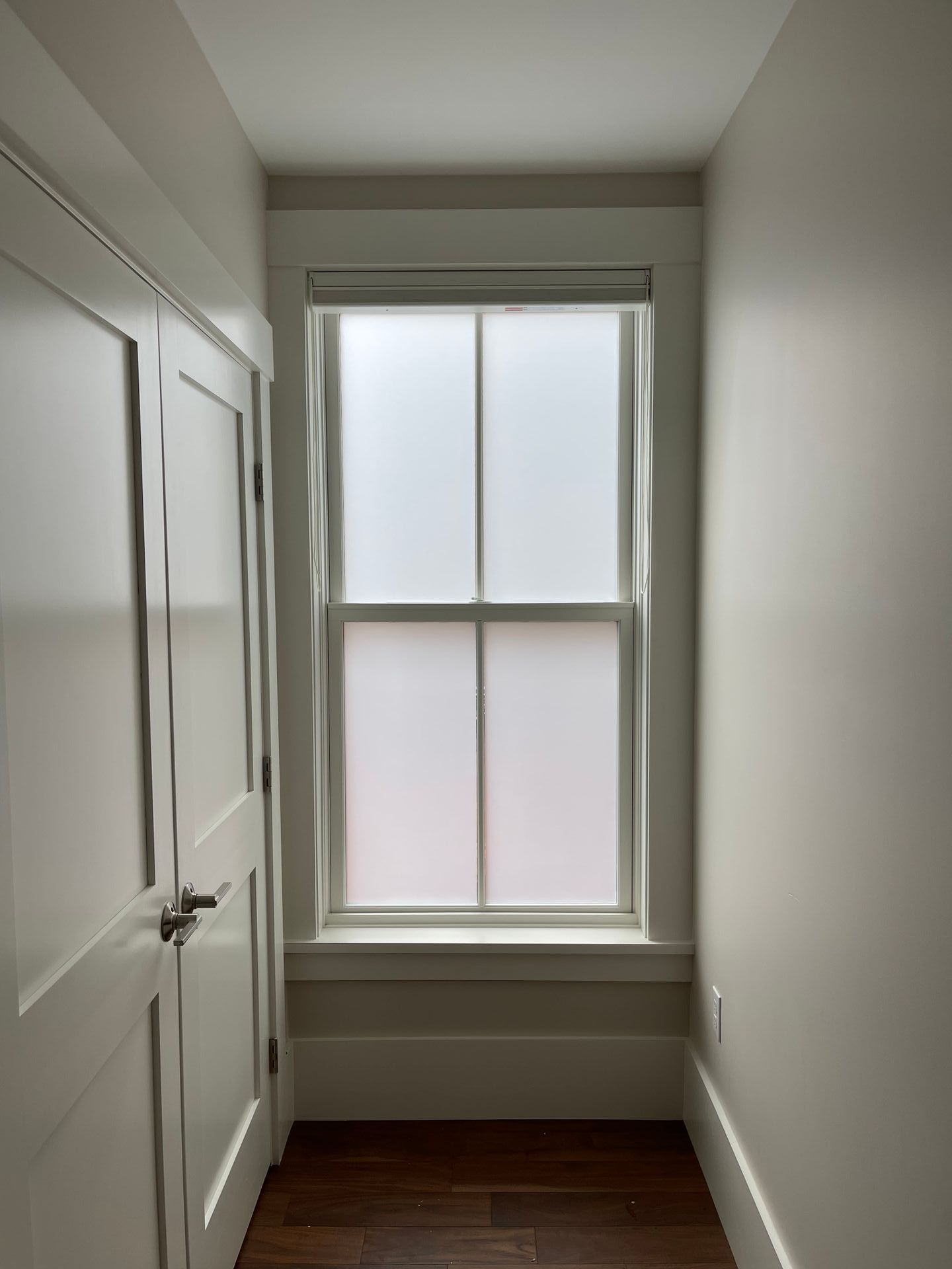 Narrow hallway with a frosted window and a white door on the left side.