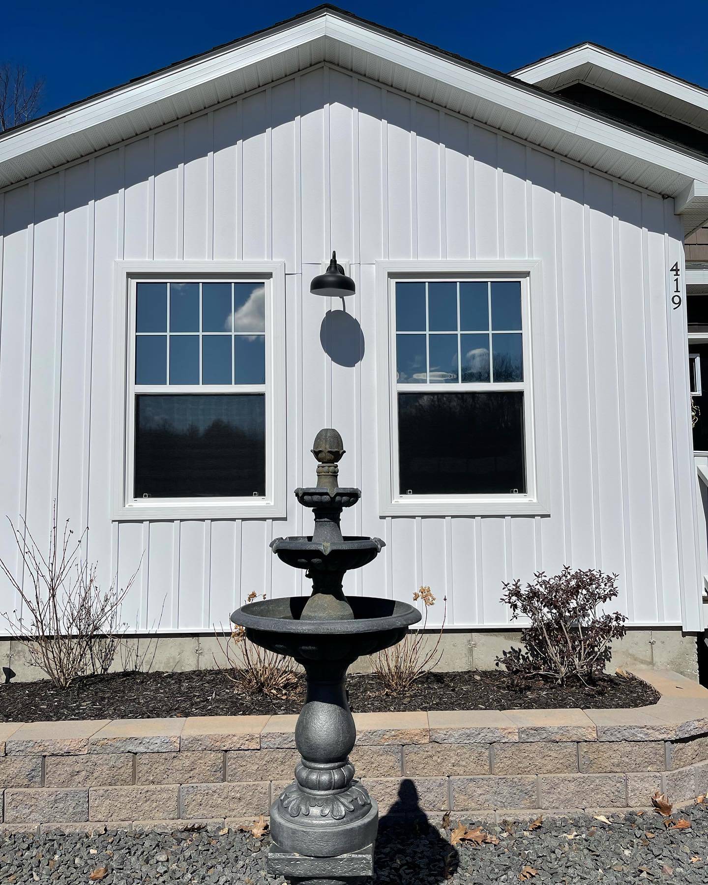 White farmhouse with windows, a fountain, and a wall-mounted light.