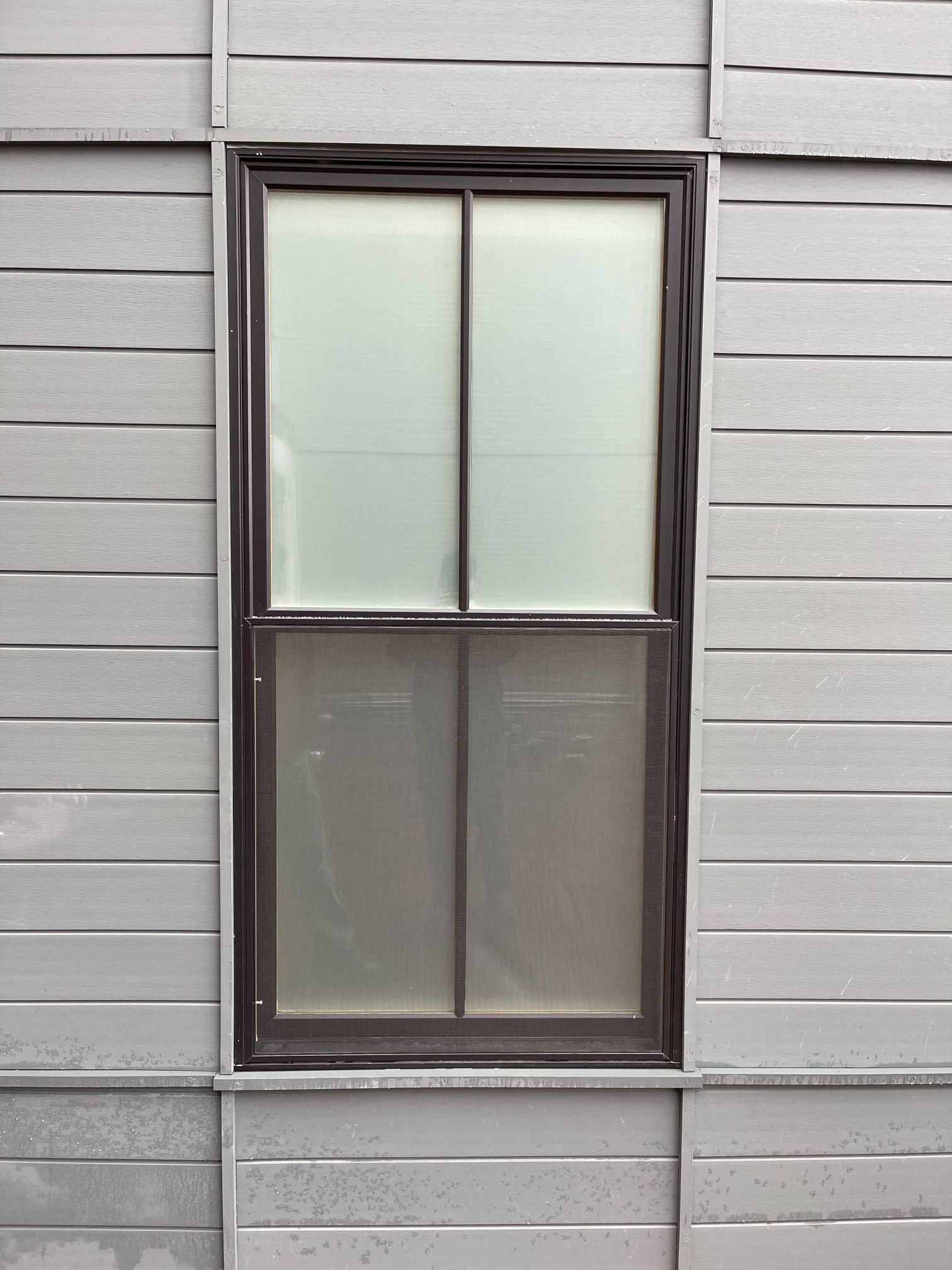 Tall, rectangular window with two panes, in a brown frame, set into a gray, horizontally-paneled wall.