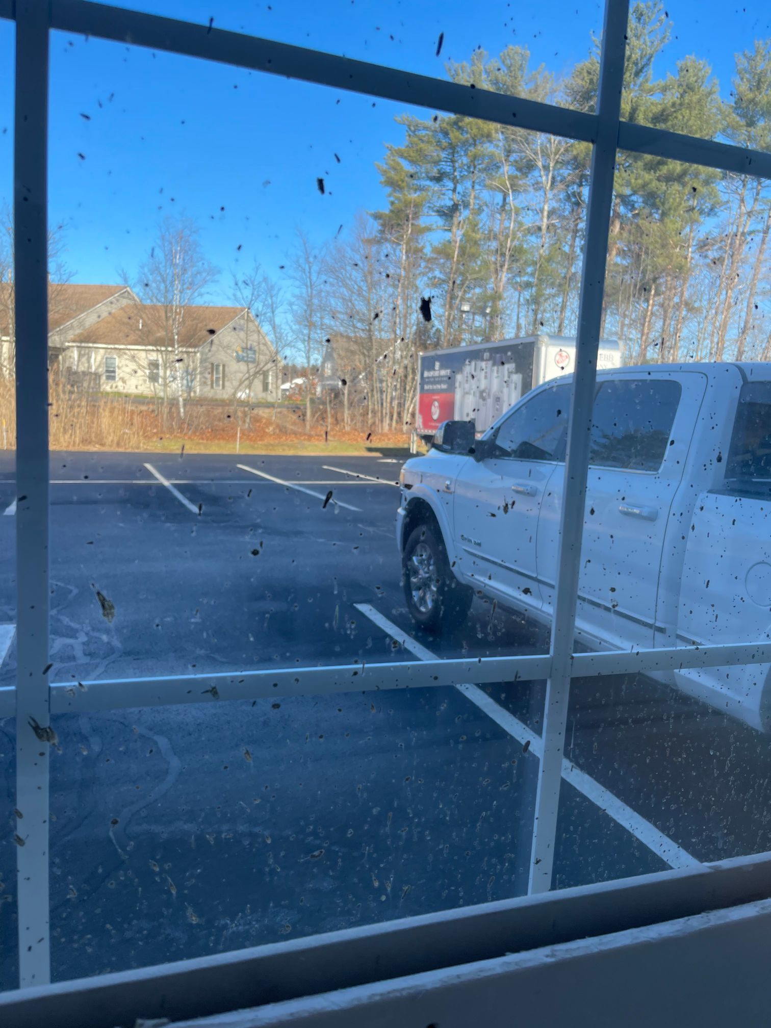 View through a dirty window of a parking lot and a white truck on a sunny day.