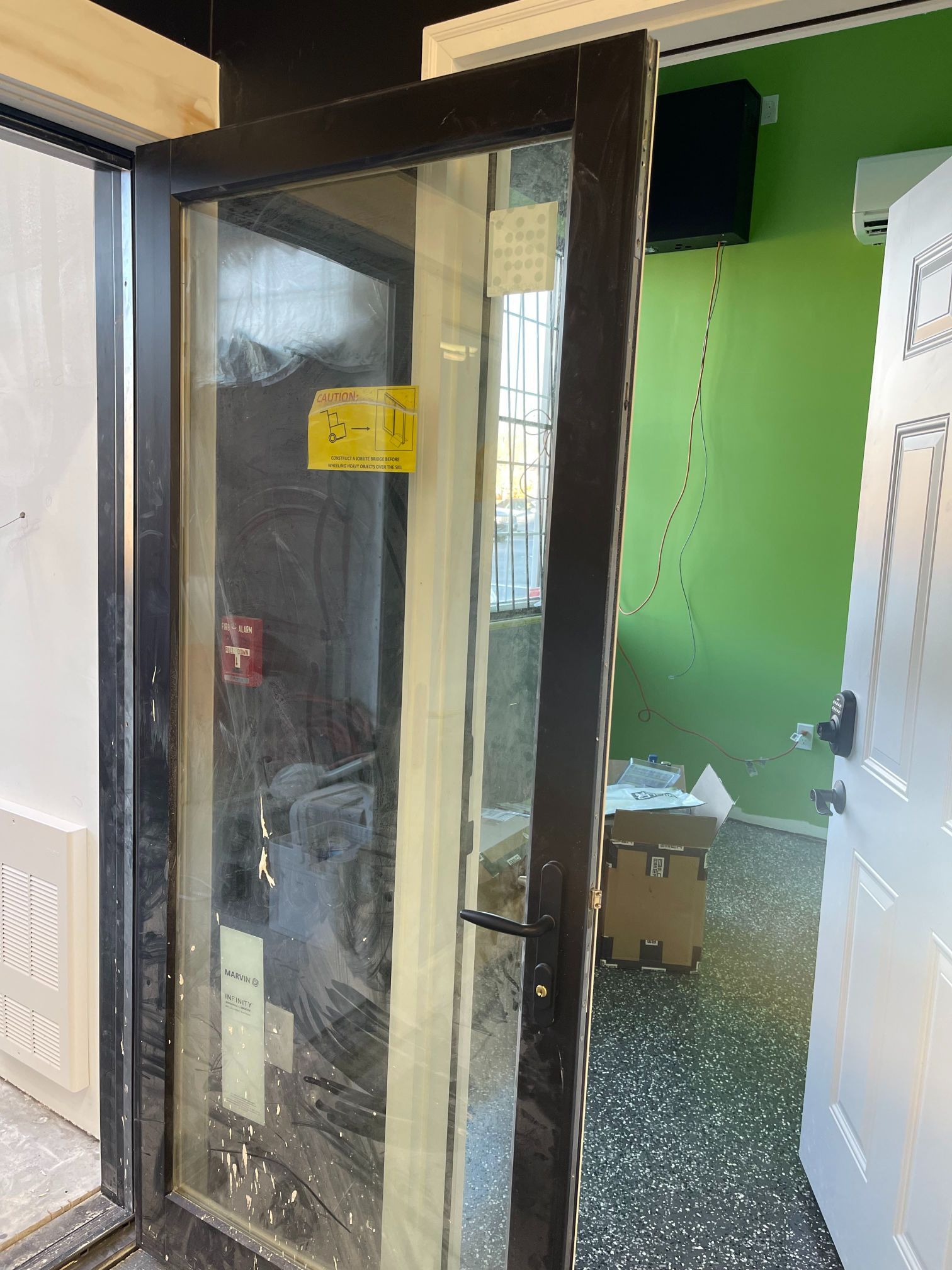 Open glass door, black frame, revealing interior with green wall, boxes, and white door.