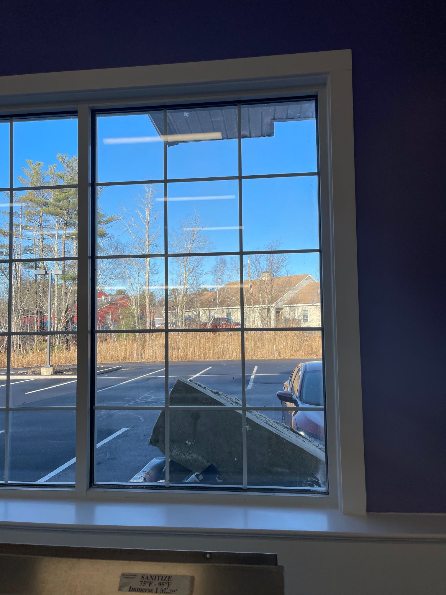 Window with grid panes overlooking a parking lot and a building with blue sky.