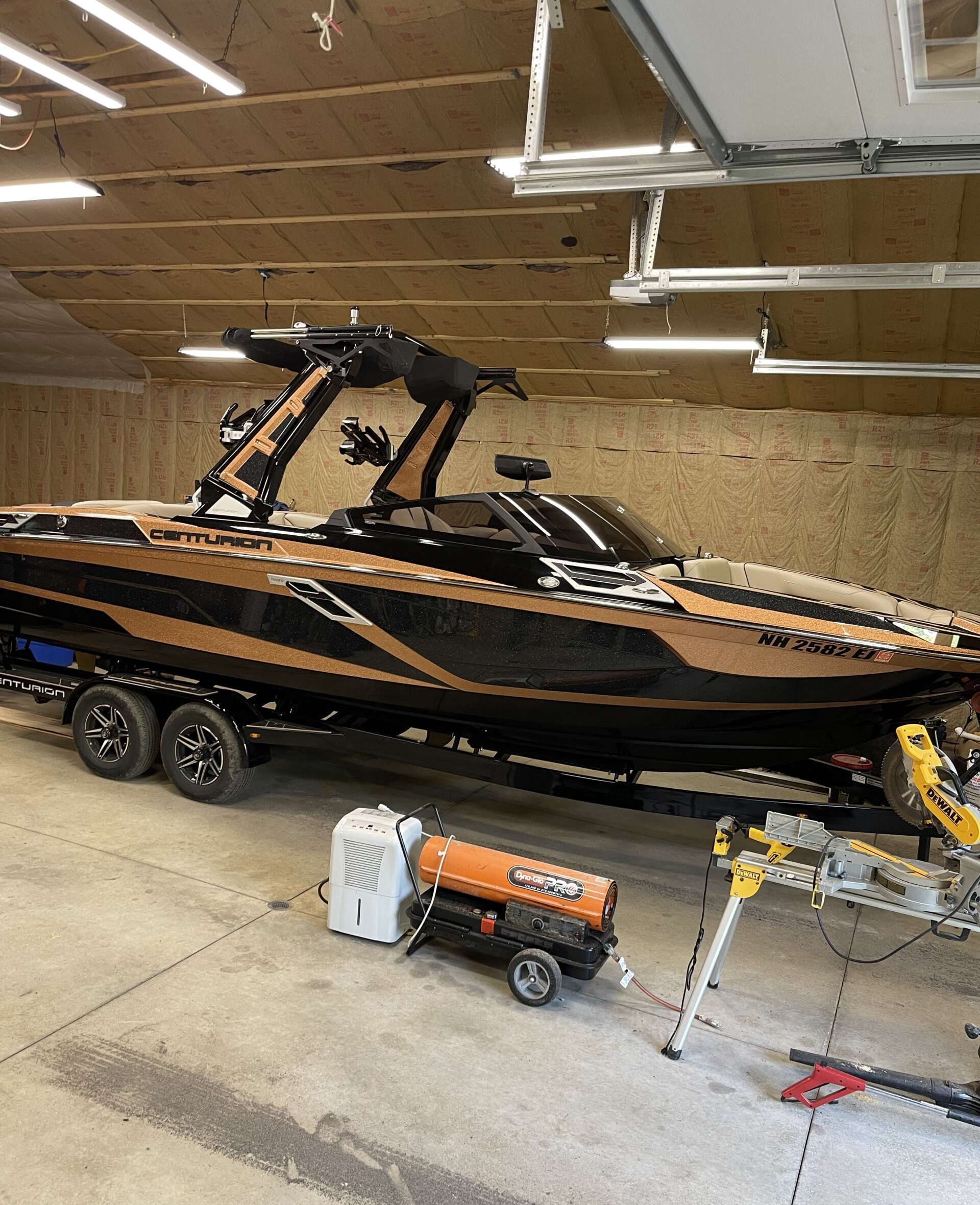 A large, black and bronze boat on a trailer inside a garage with equipment.