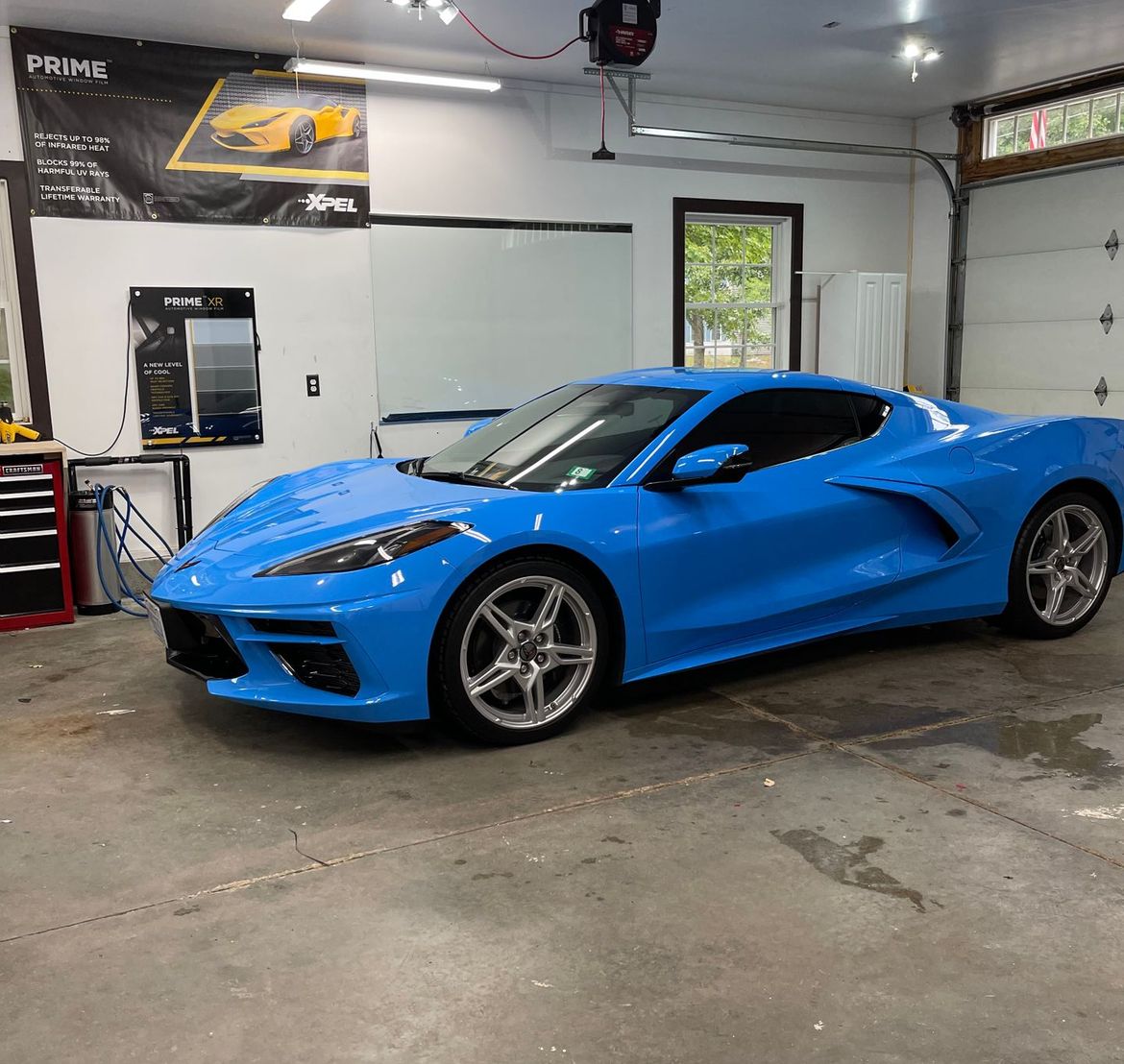 Blue Corvette sports car inside a garage with tinted windows and overhead lighting.