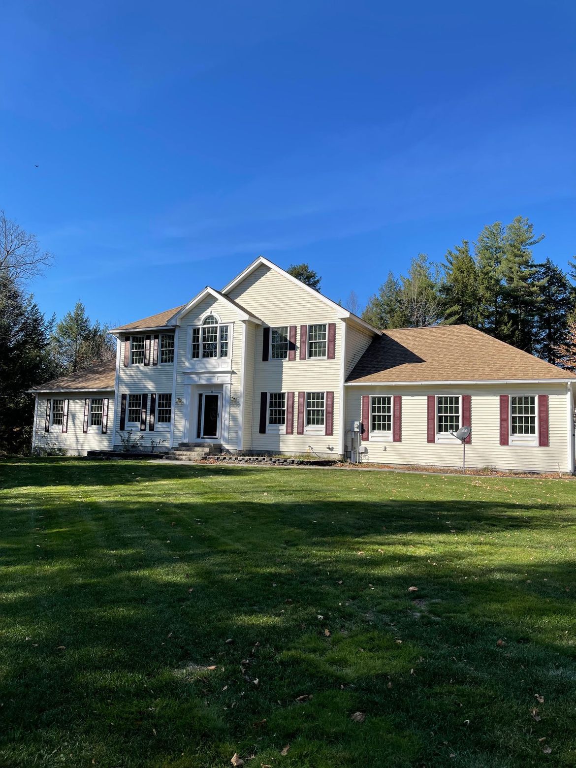 White two-story house with red shutters on a green lawn under a blue sky.