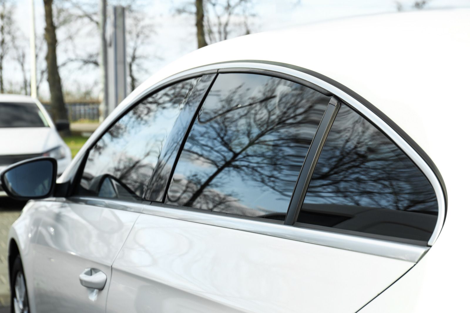 White car with tinted windows; side view, trees reflected in the glass.