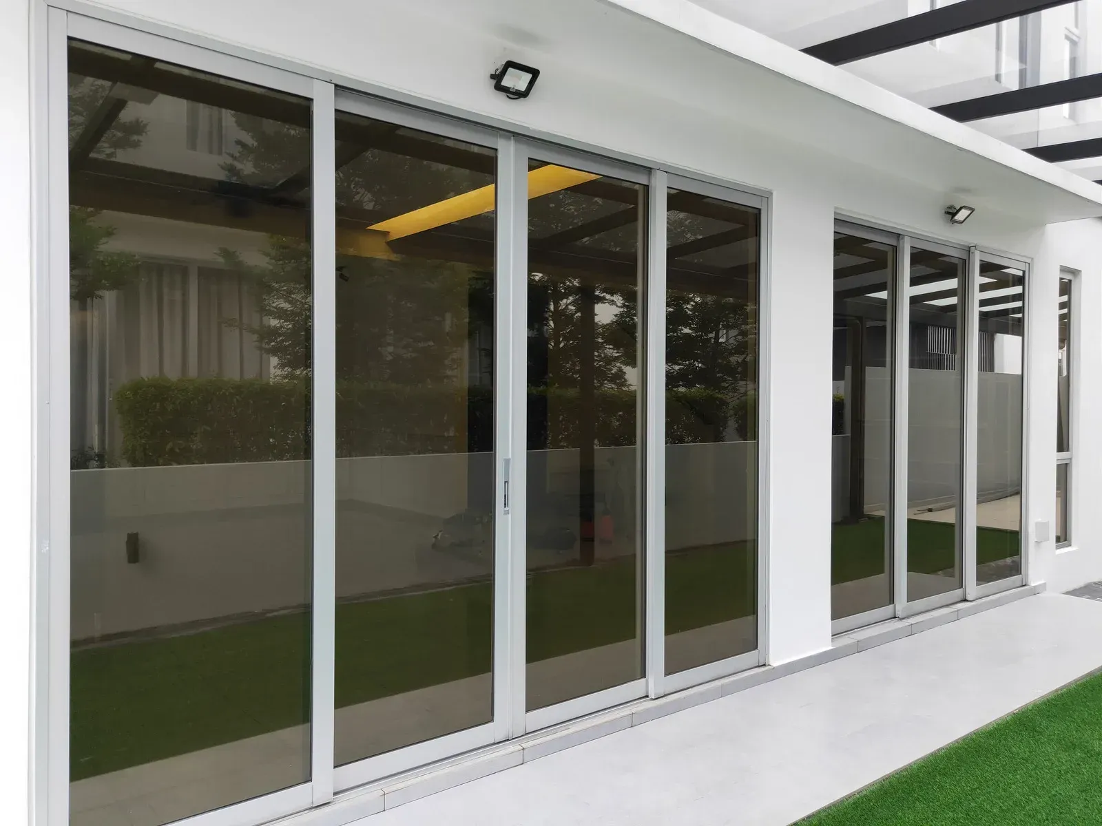 Glass sliding doors with silver frames on a white building, reflecting the outside.