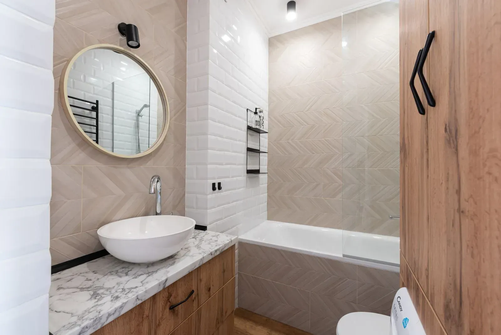 Bathroom with wood vanity, marble counter, round mirror, and bathtub with white subway tiles.