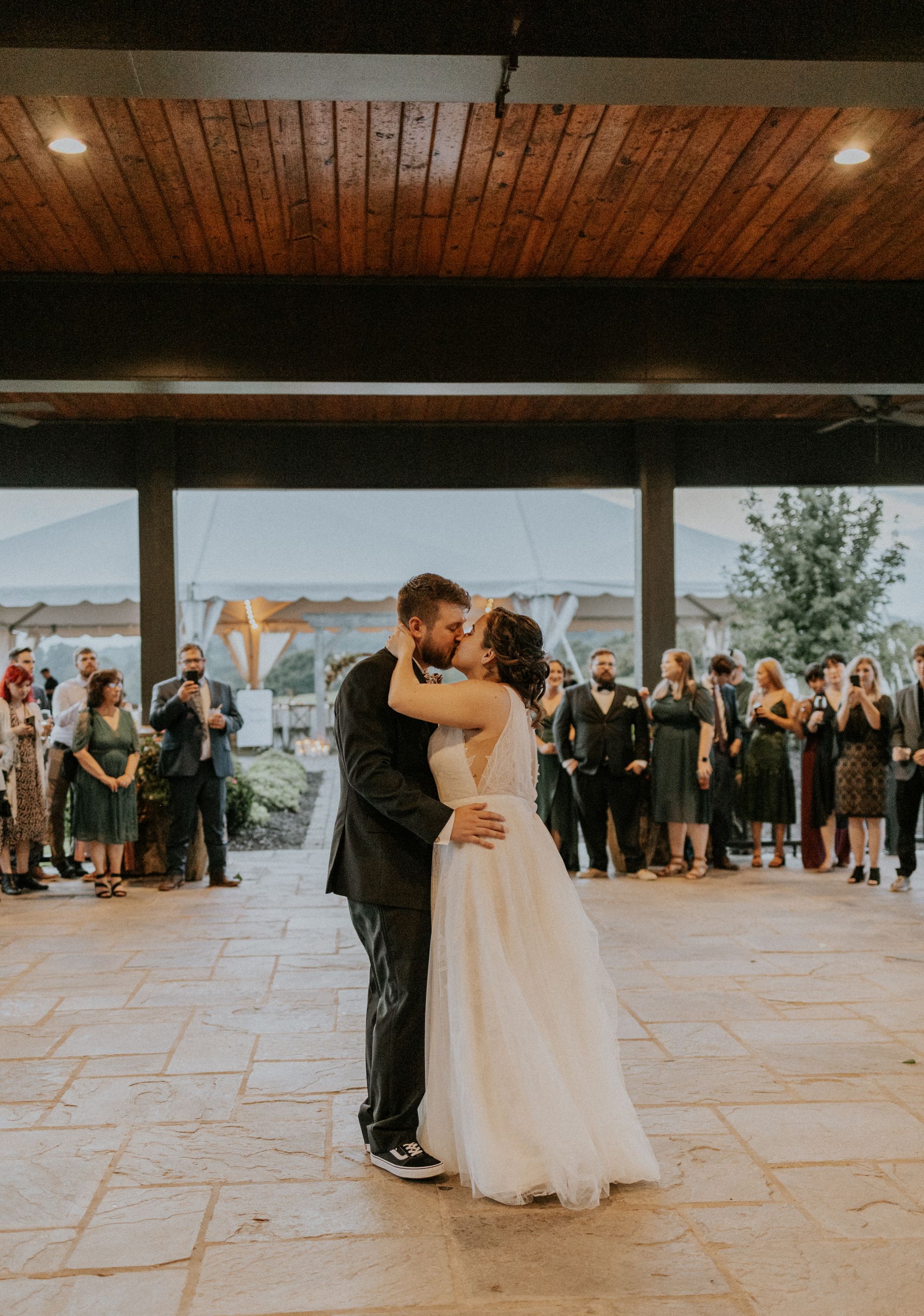 Bride and groom kissing on dance floor at outdoor reception; guests watch.