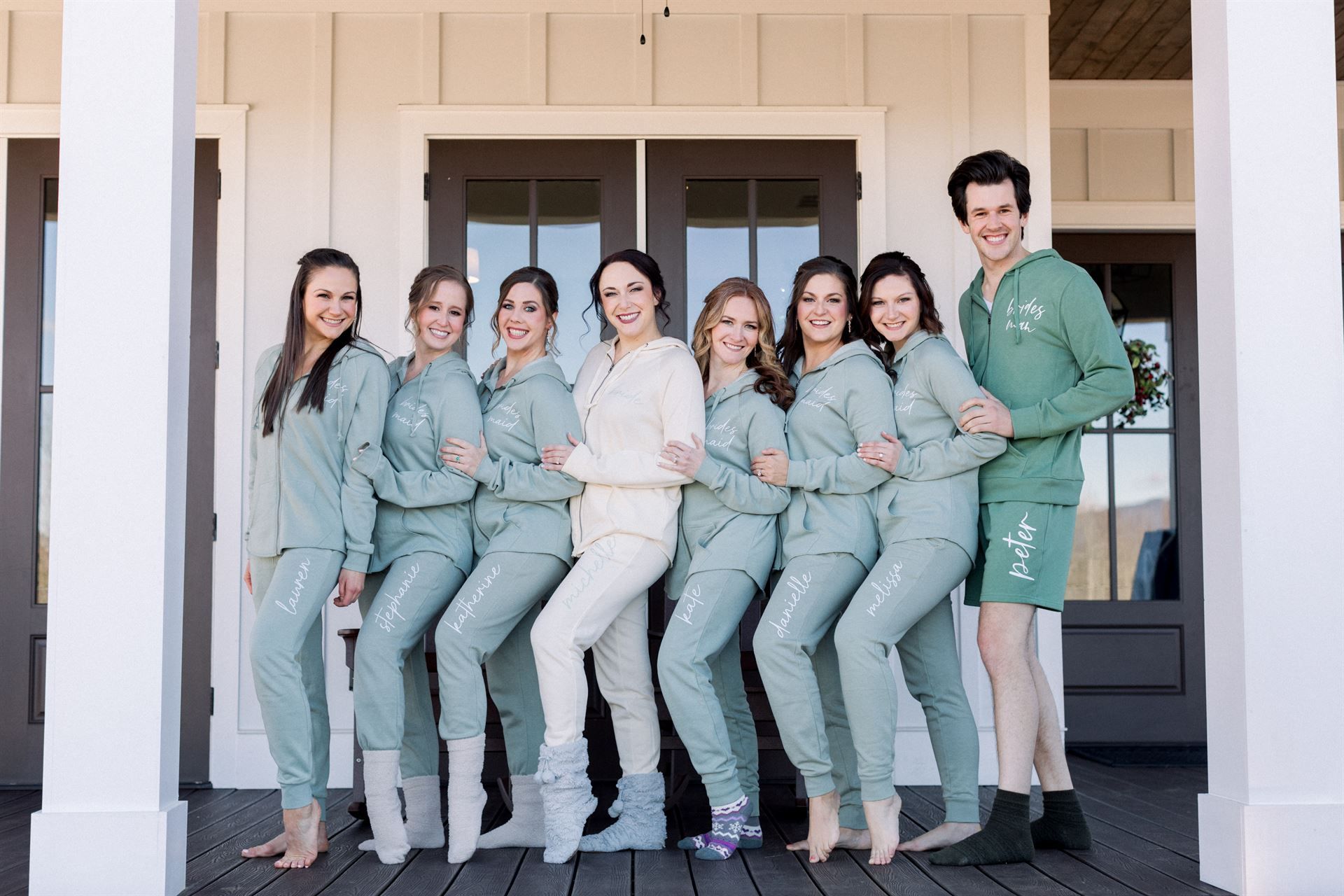 Group of people in matching green pajamas posing on a porch. One person wears cream-colored pajamas.